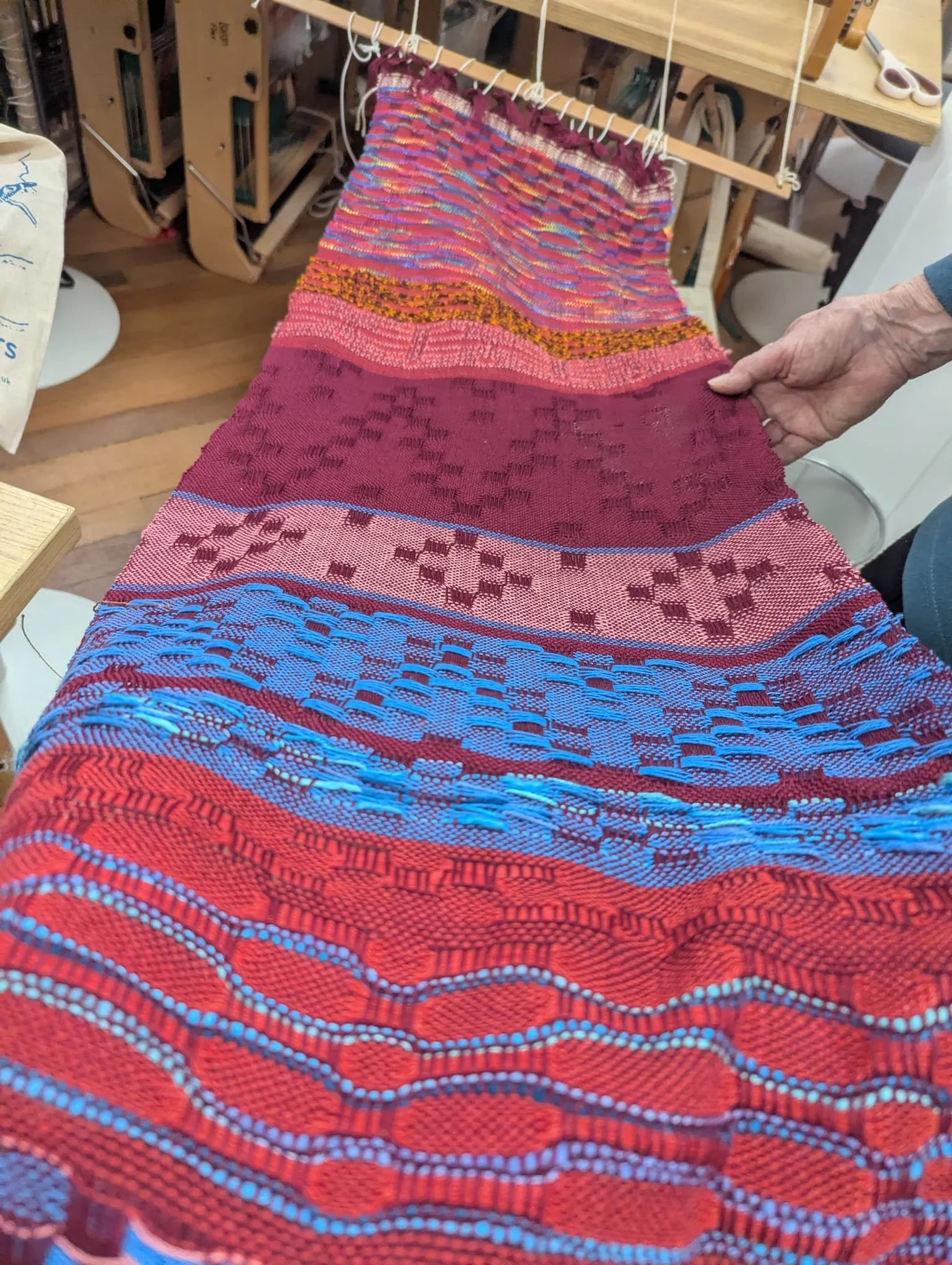 Colorful woven textile with geometric patterns in pink, blue, red, and orange displayed on a table.
