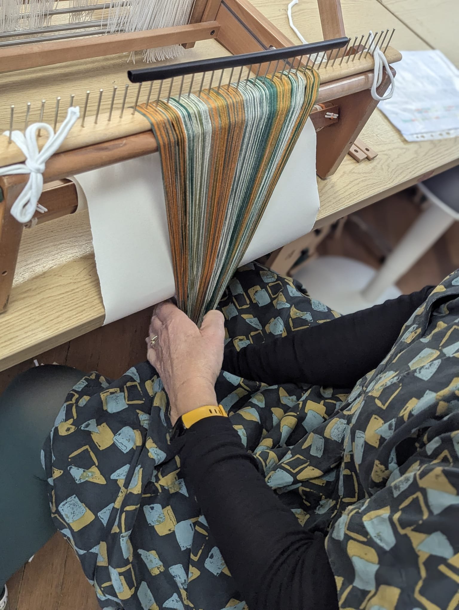 Person weaving colorful yarn on a loom.