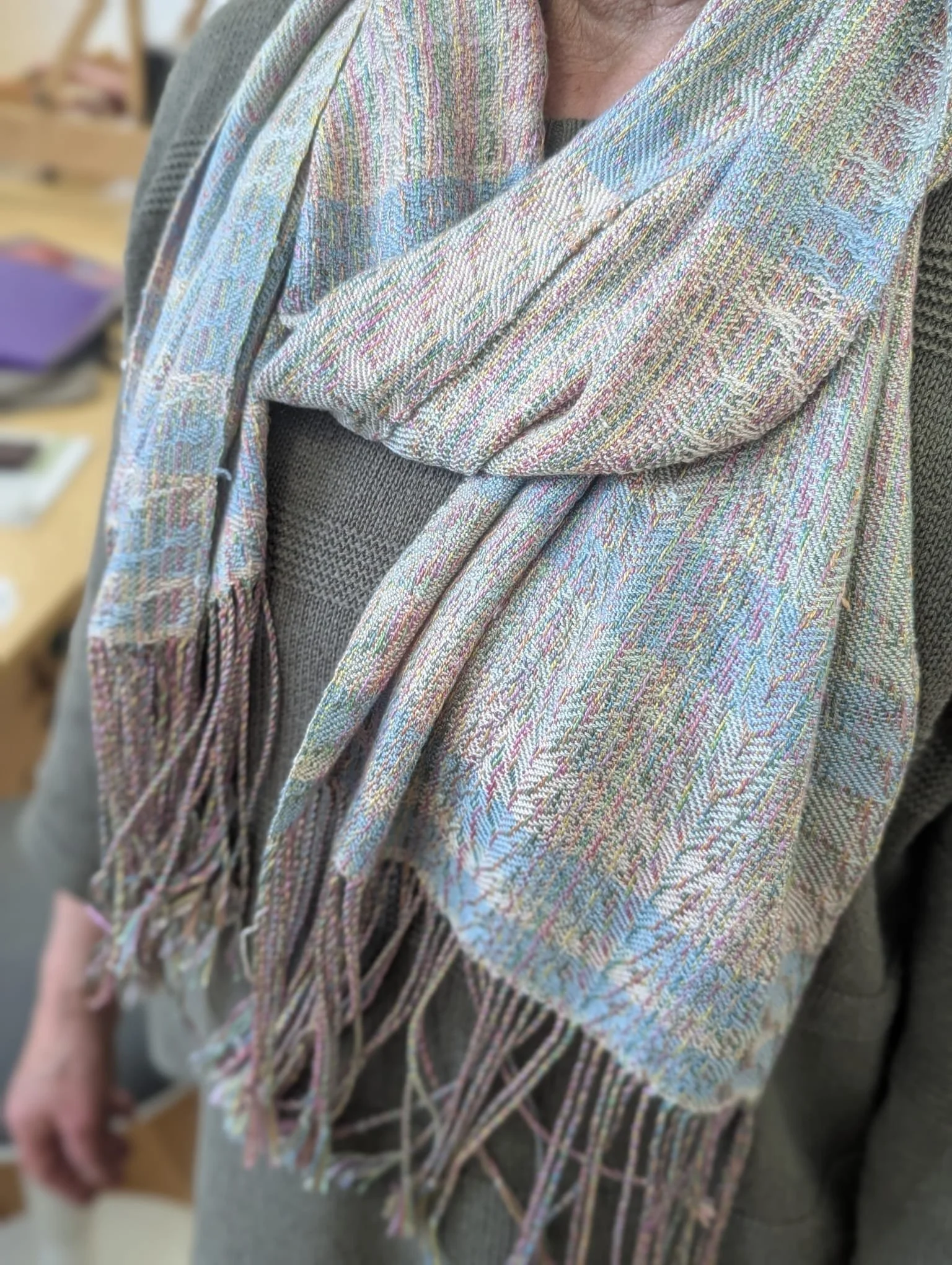 Close-up of a person wearing a multicolored woven scarf with fringes, over a gray sweater.