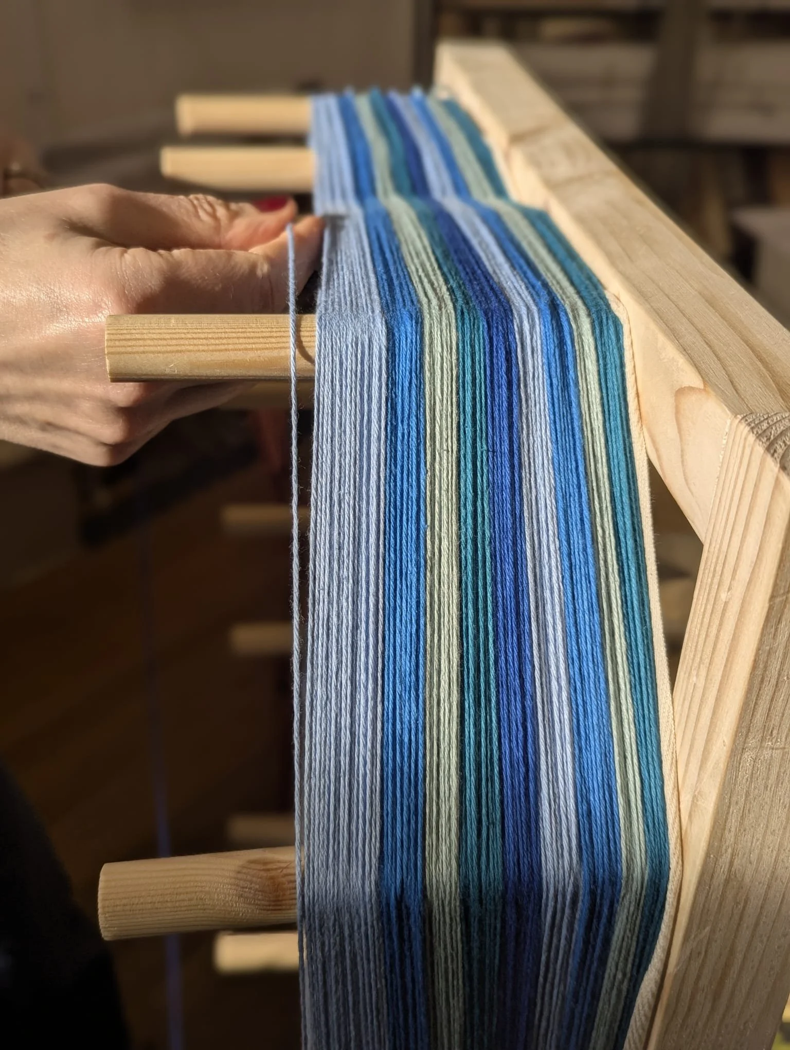 Close-up of a person weaving colorful yarn on a wooden loom, with shades of blue and green.