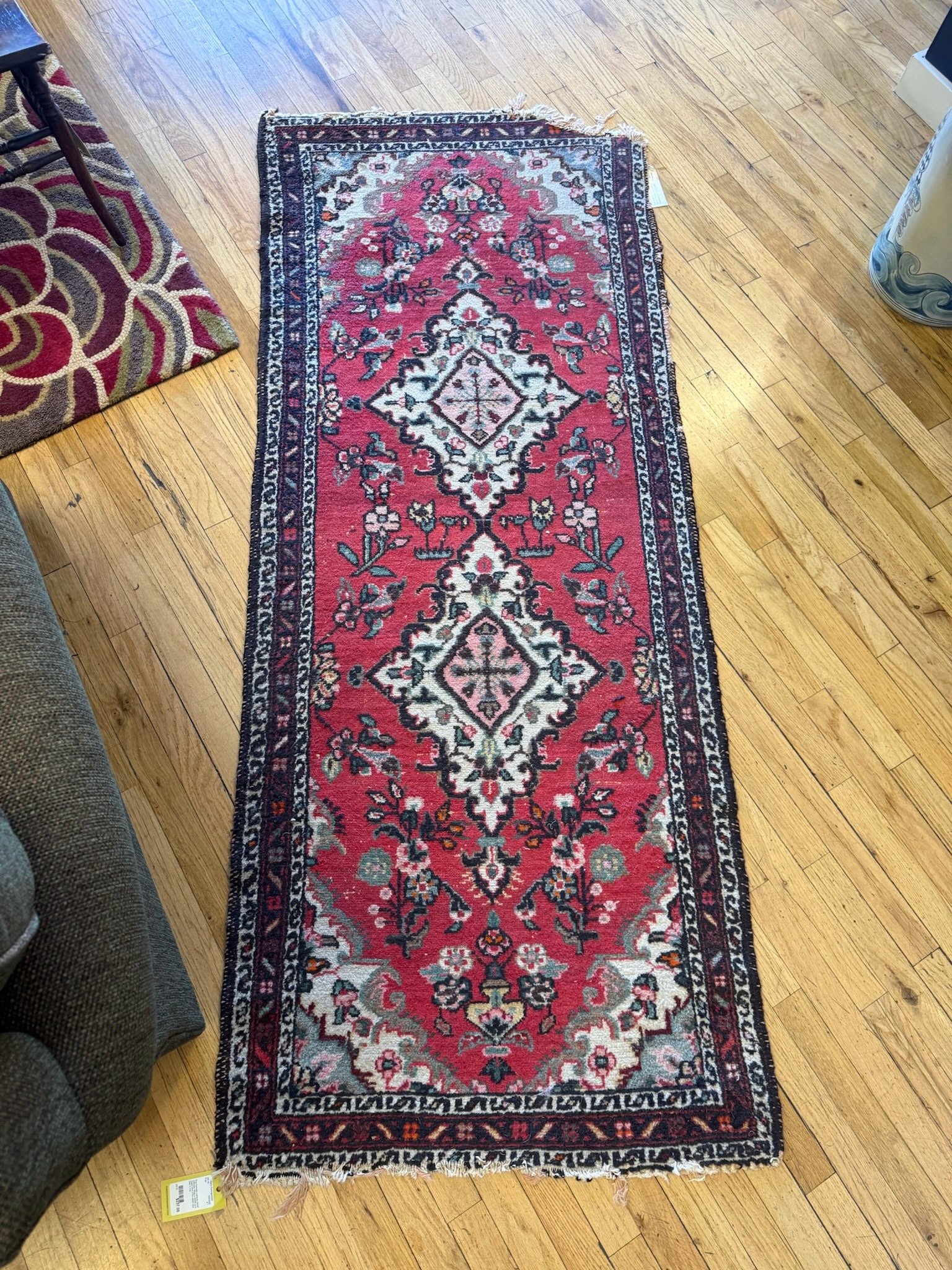 A long, rectangular Persian-style rug with a red background and intricate black, white, pink, green, and blue floral and geometric patterns