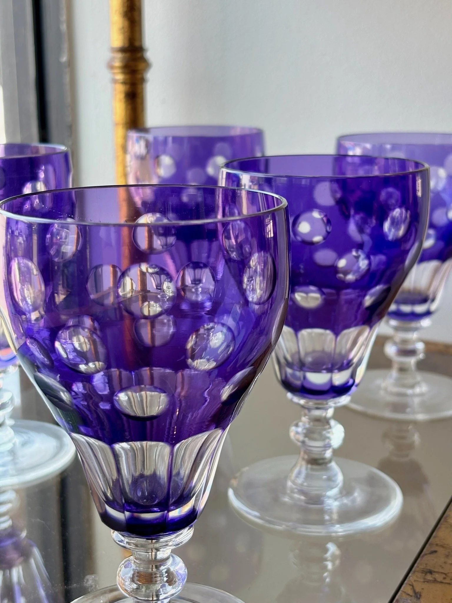 A set of purple and clear glass goblets with bubble-like patterns, arranged on a reflective surface.
