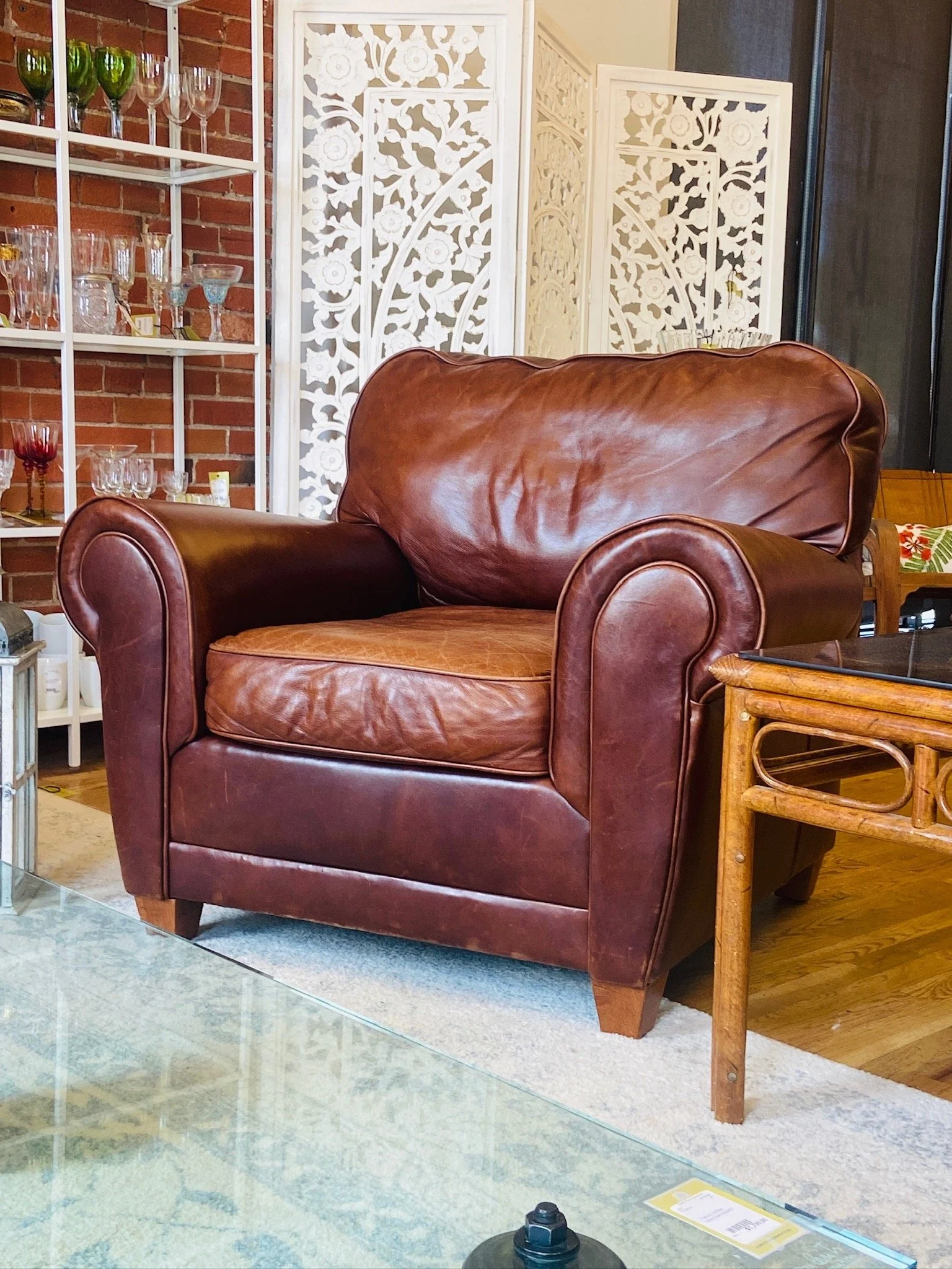 A brown leather armchair in a room with a brick wall, decorative white panels, and a display shelf with wine glasses and glassware.