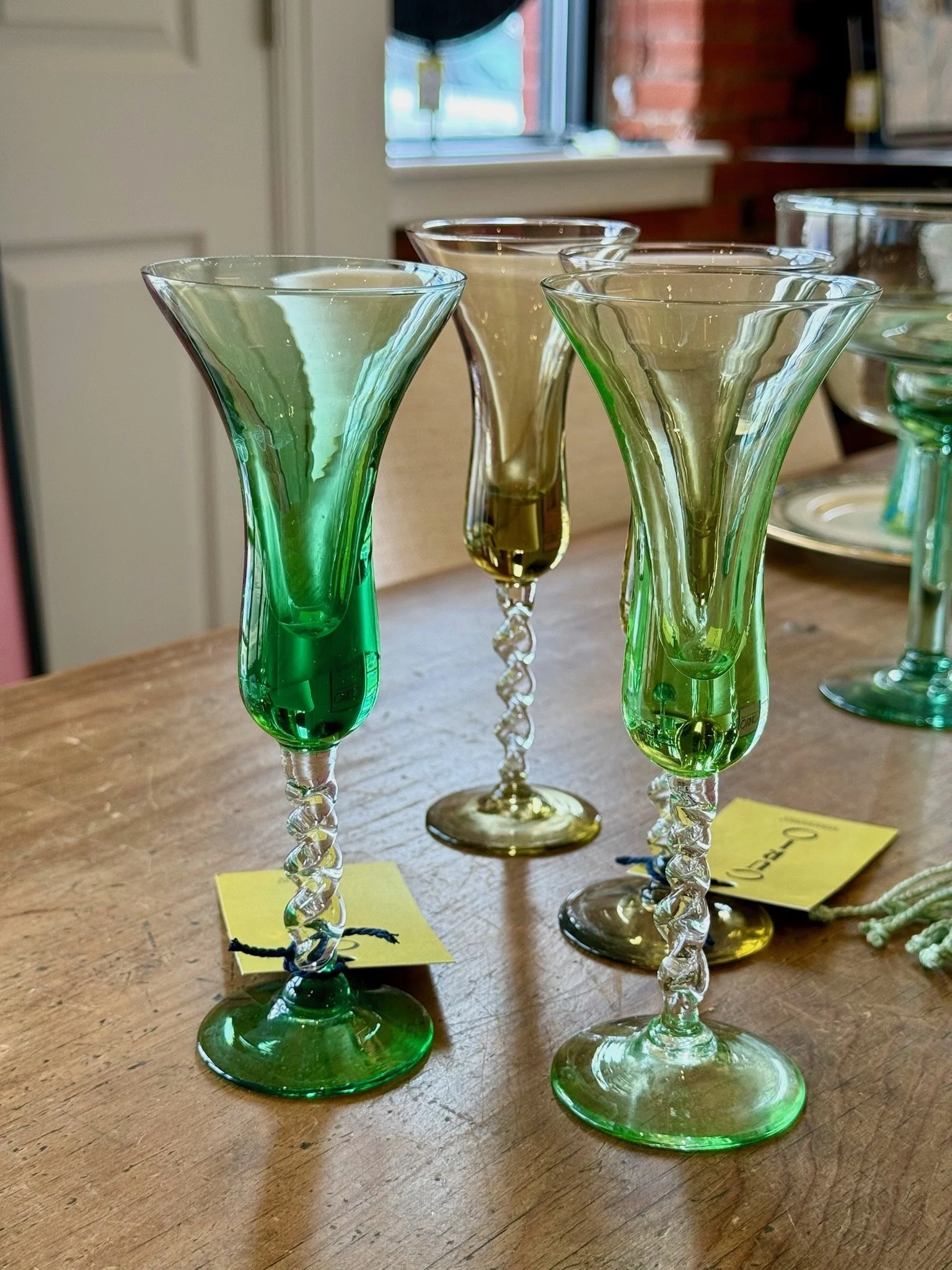 A set of decorative glass vases with spiral stems, some green and some clear, arranged on a wooden table near a window.