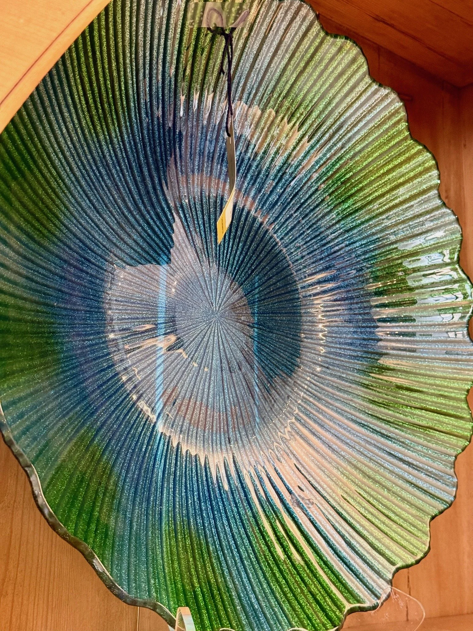 A decorative glass bowl shaped like a leaf, with green, blue, and gold colors, placed on a wooden surface.