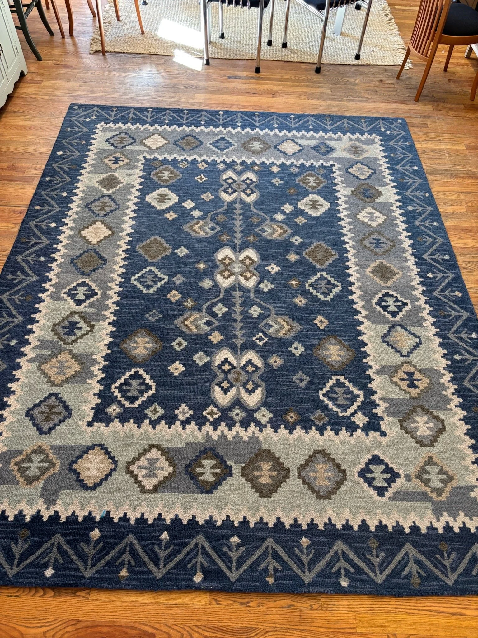 A large rectangular area rug with a traditional geometric pattern in blue, beige, gray, and white tones,