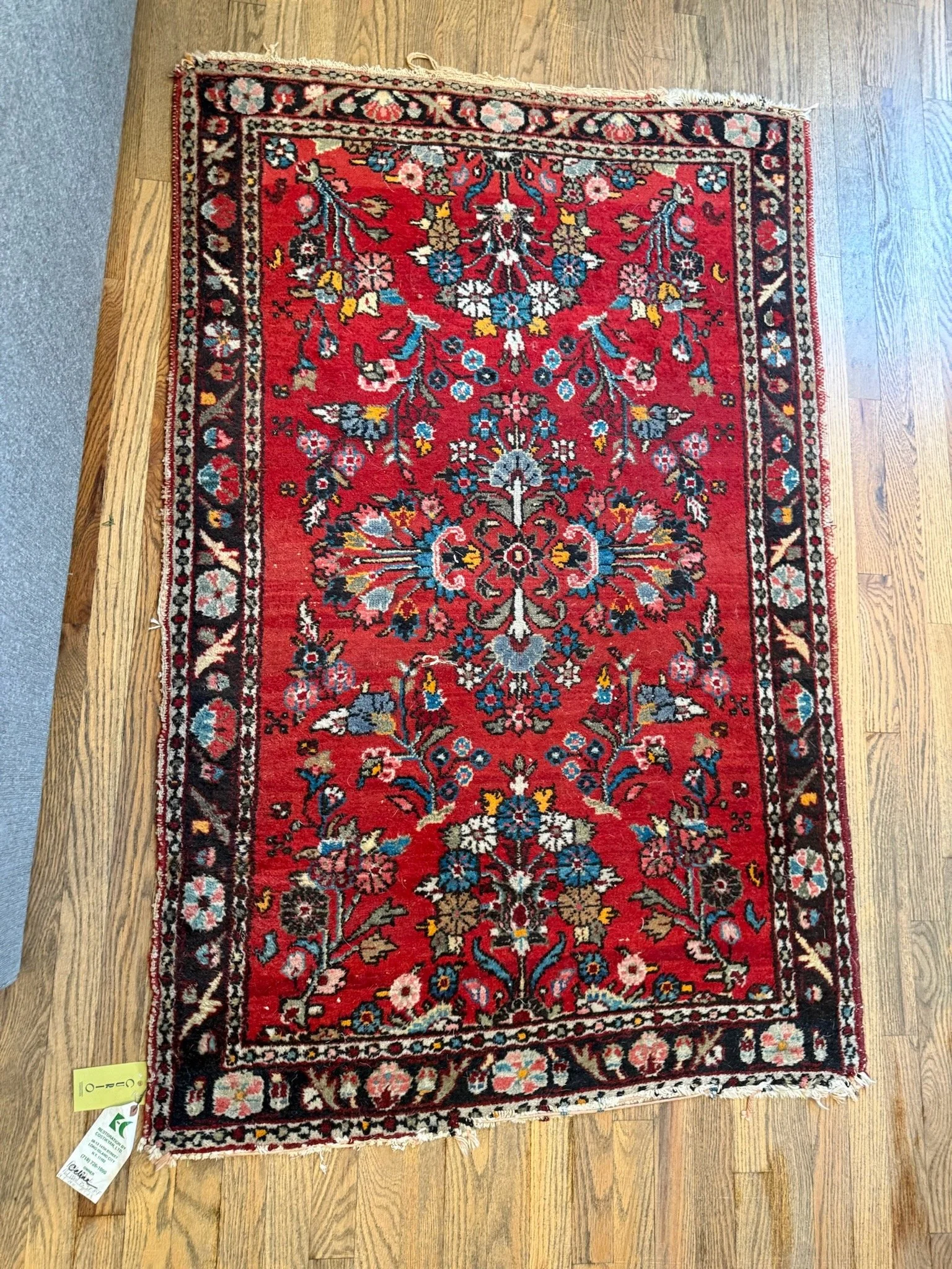 A rectangular red Oriental rug with intricate floral patterns and black, pink, blue, and yellow accents