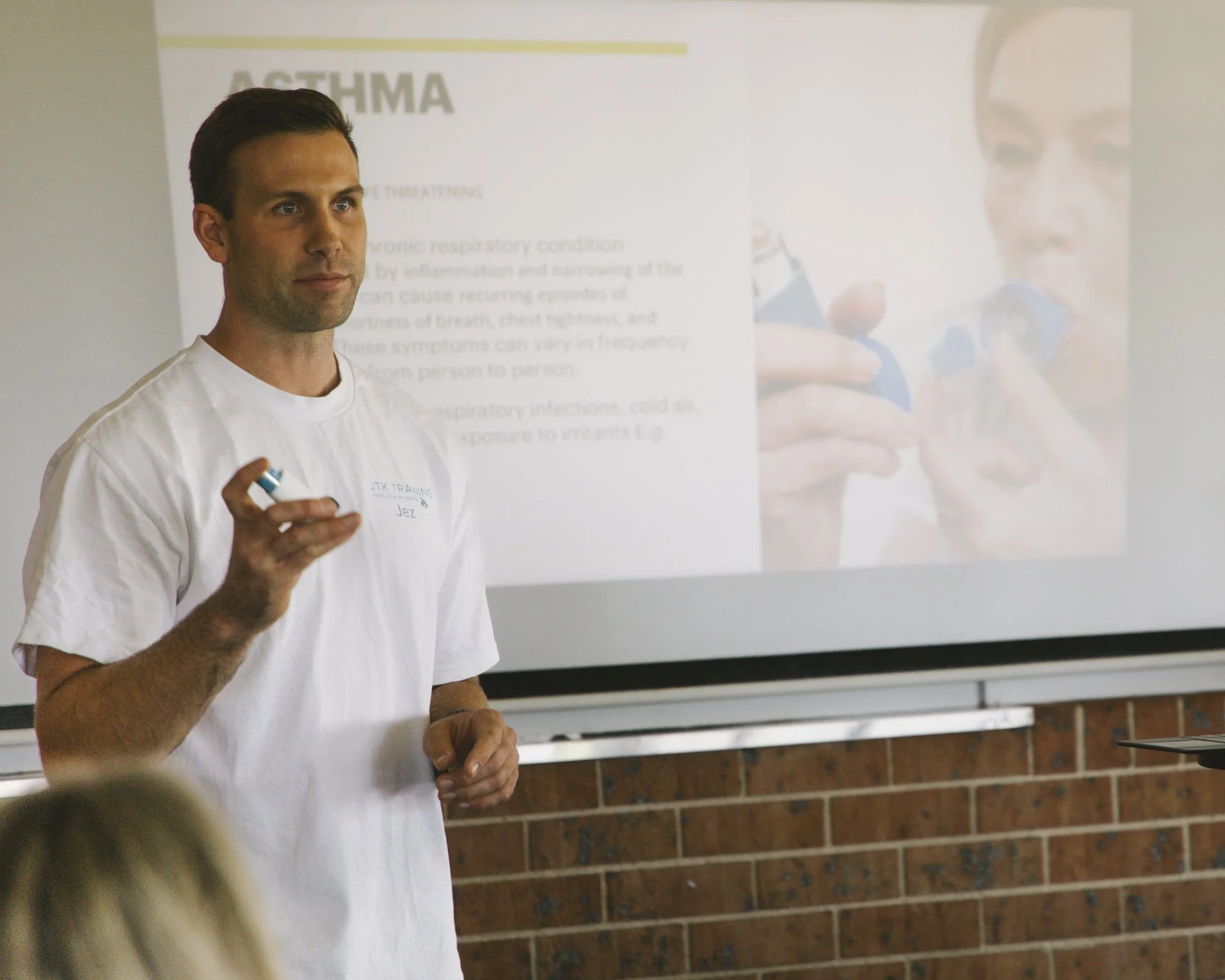 Man giving a presentation on asthma in front of a projected slide showing a person using an inhaler.