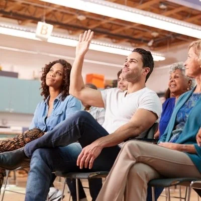 People seated in a classroom, one raising hand to ask a question.