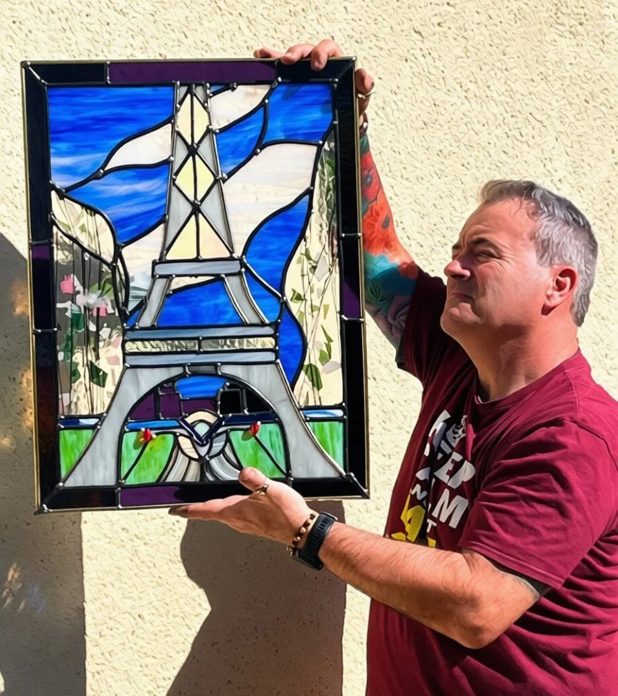 David displaying completed Eiffel Tower stained glass panel outdoors 
