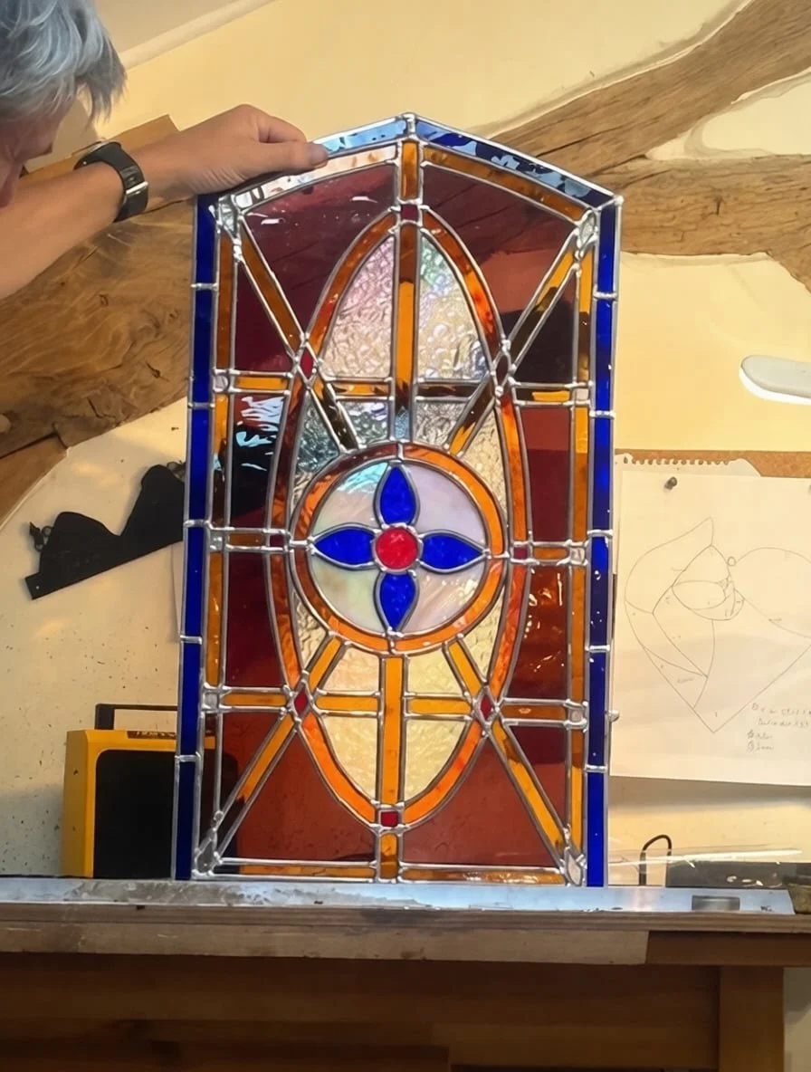 Stained glass farm door window panel on workshop table showing traditional lead came construction with amber and burgundy glass