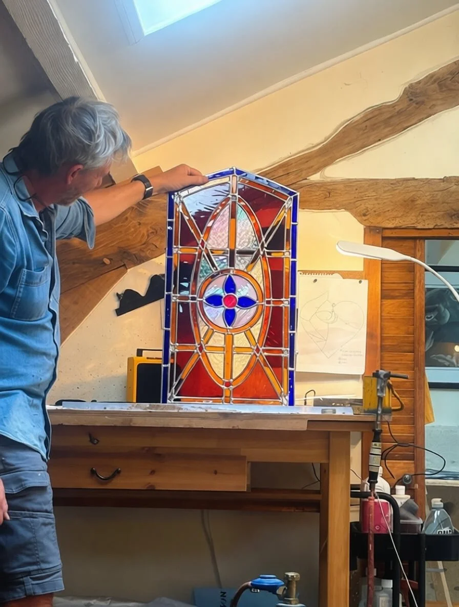 Artist inspecting completed farm door stained glass window showing blue border and opalescent center medallion
