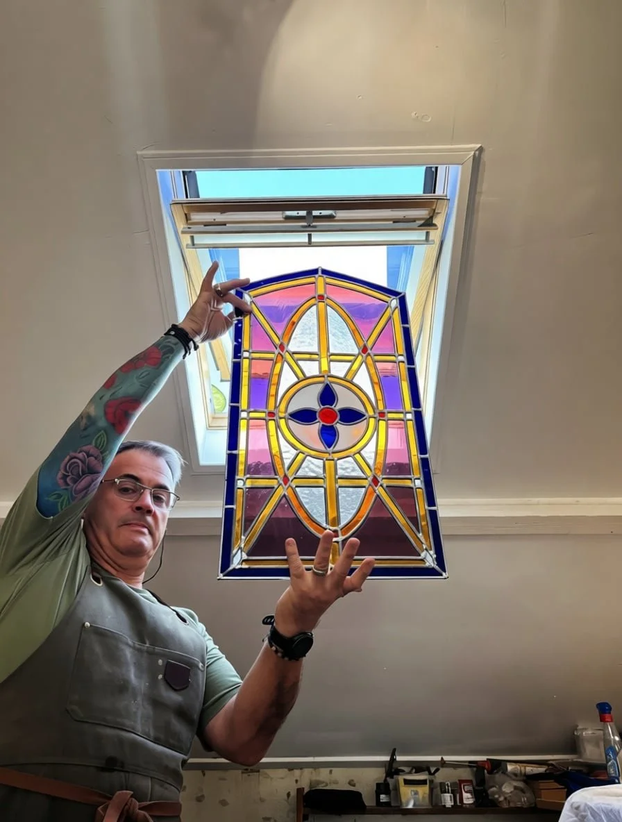 Completed farm door stained glass window held up to light showing vibrant pink, blue, and amber cathedral glass