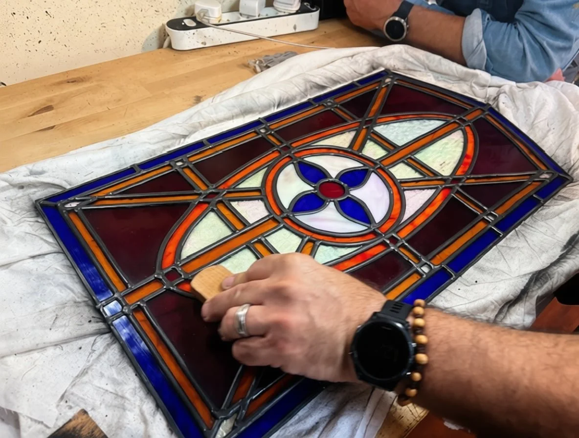 Artist hand-finishing stained glass farm door window, showing detailed lead came work and textured glass