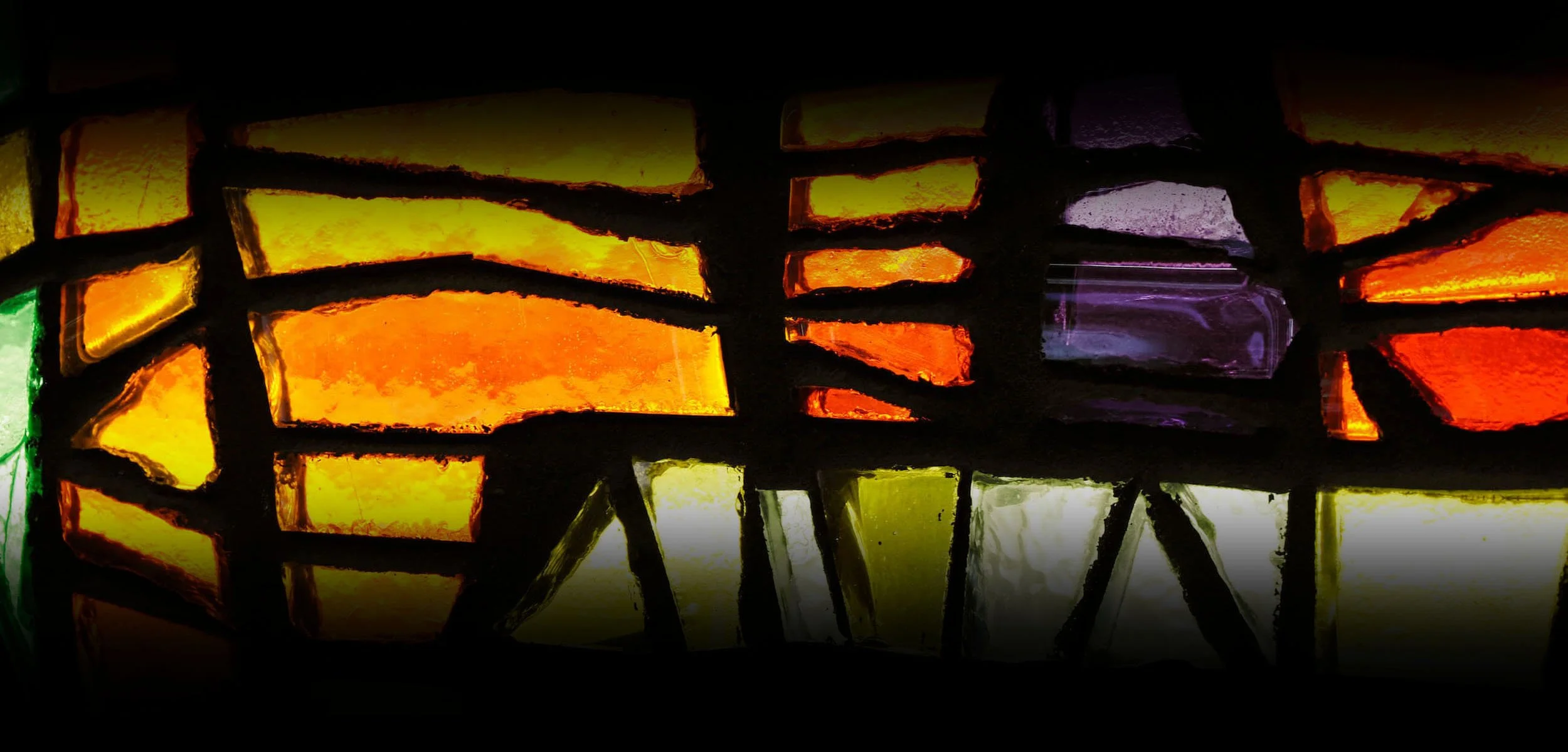 Colorful stained glass window with geometric patterns, illuminated from behind.