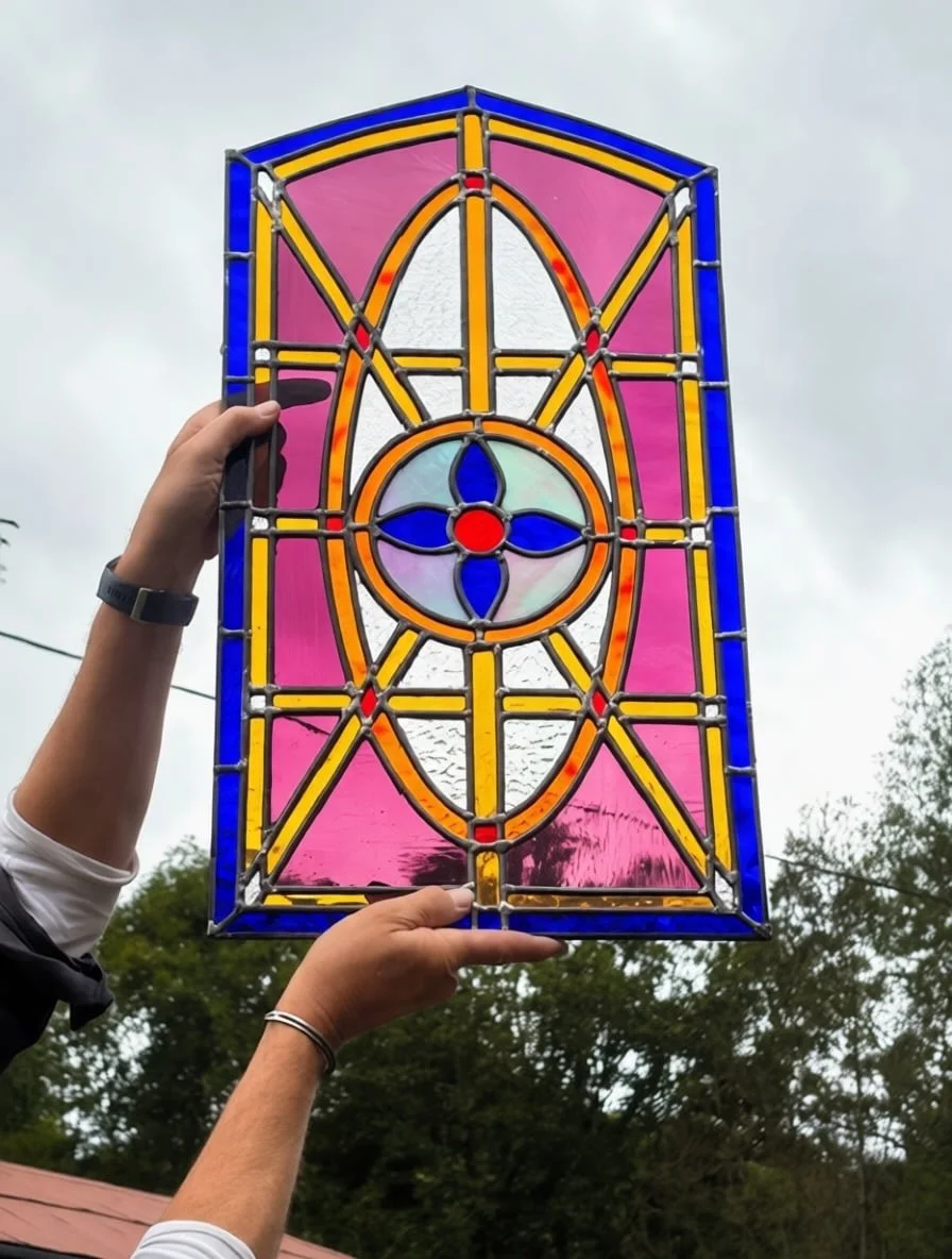 Completed farm door stained glass window held up to natural light showing vibrant pink, blue, and amber cathedral glass