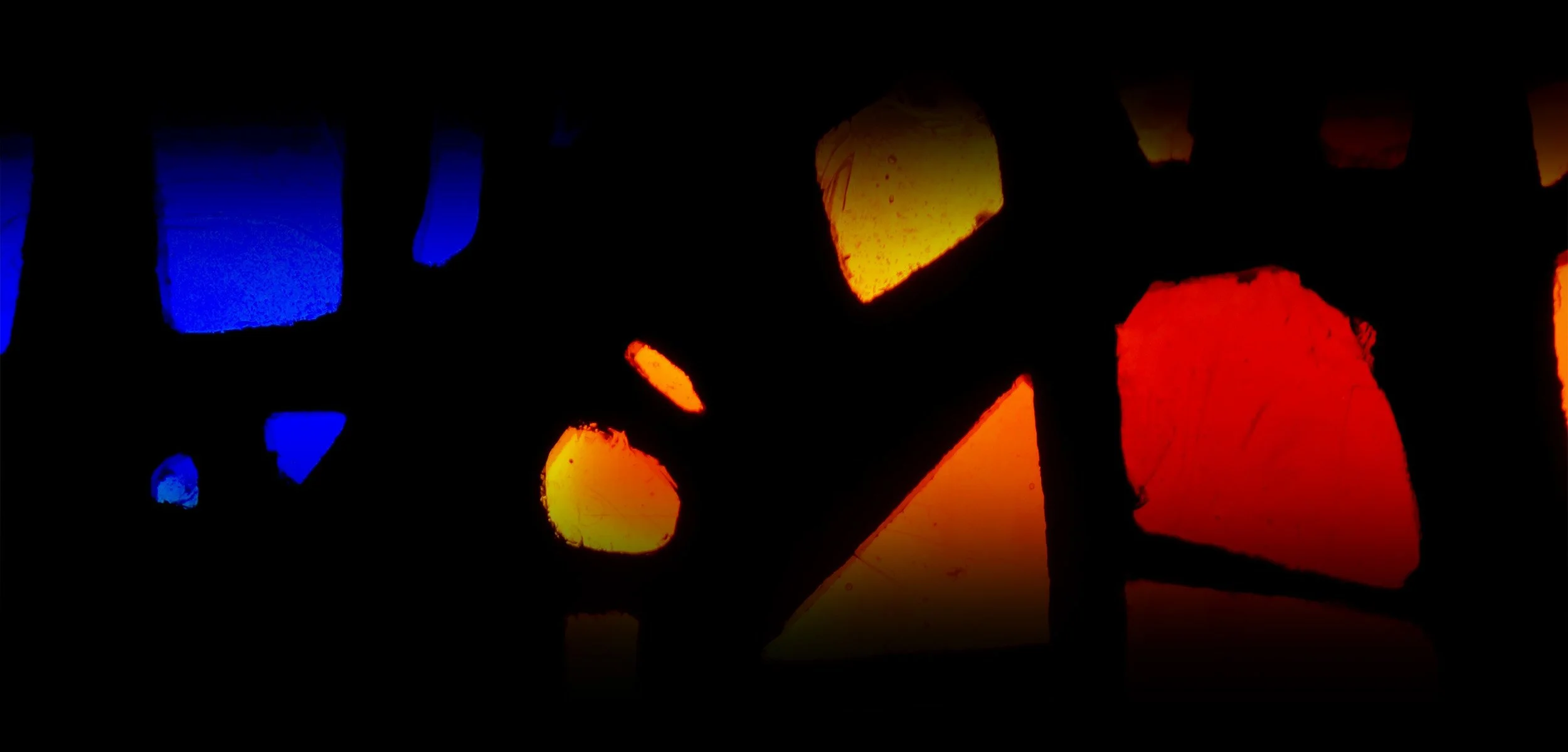 Glowing stained glass pieces in blue, yellow, orange, and red scattered against a dark background.