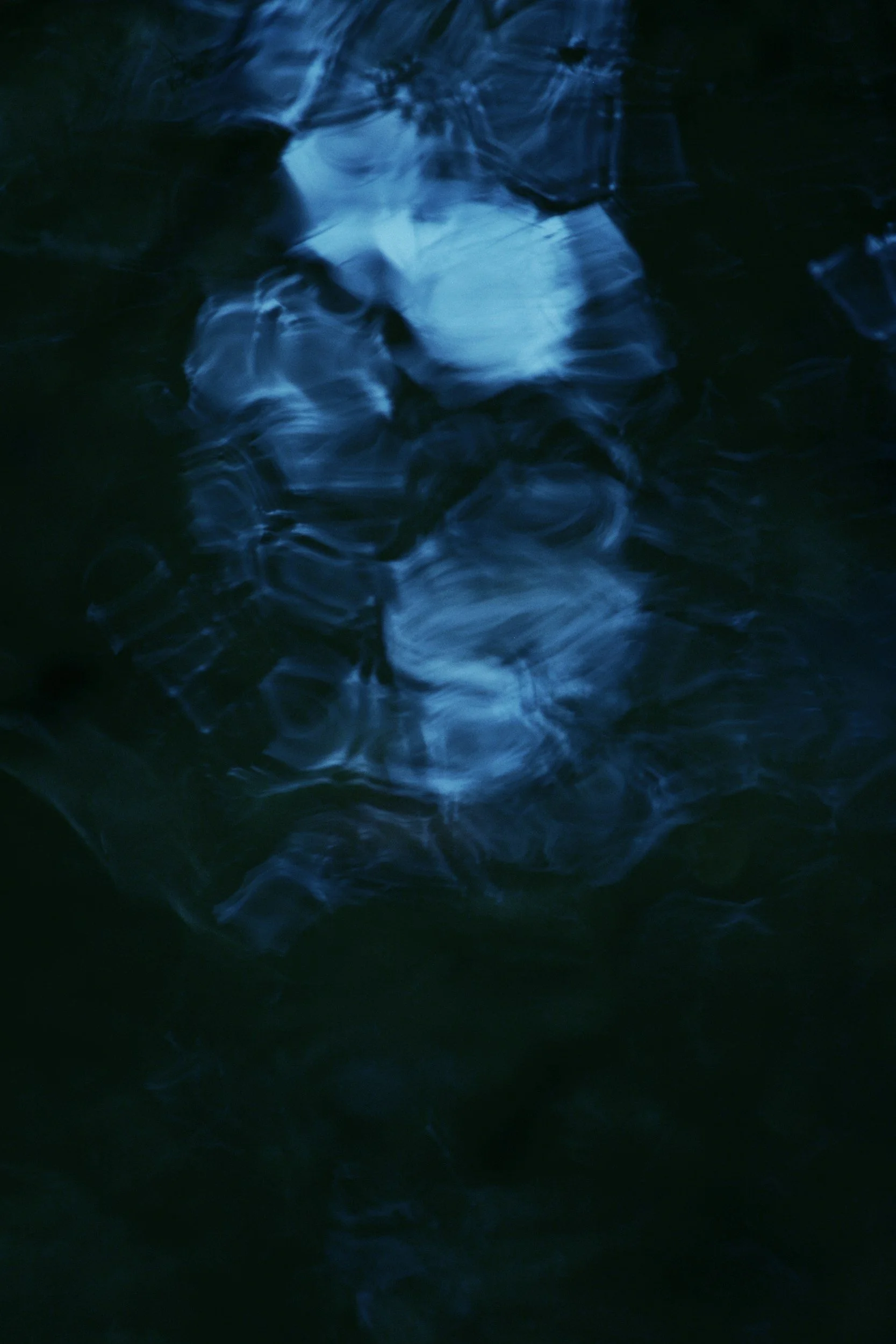 Abstract image of dark water with ripples and reflections, illuminated by blue light.