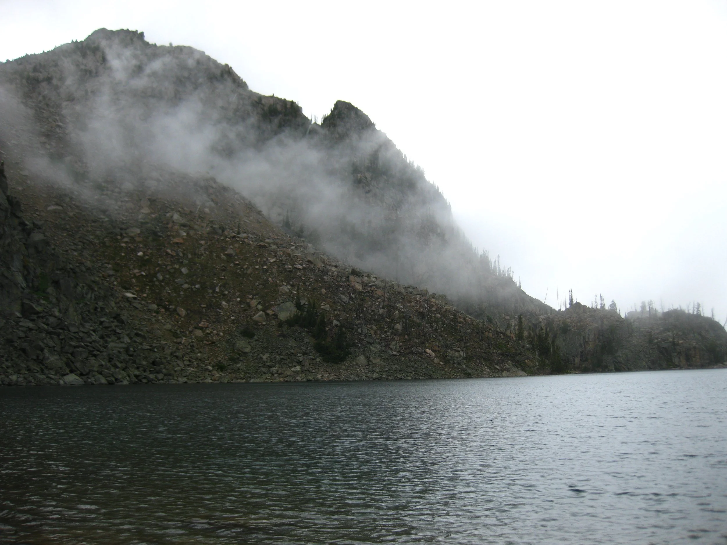 Foggy mountain landscape with a lake in the foreground.