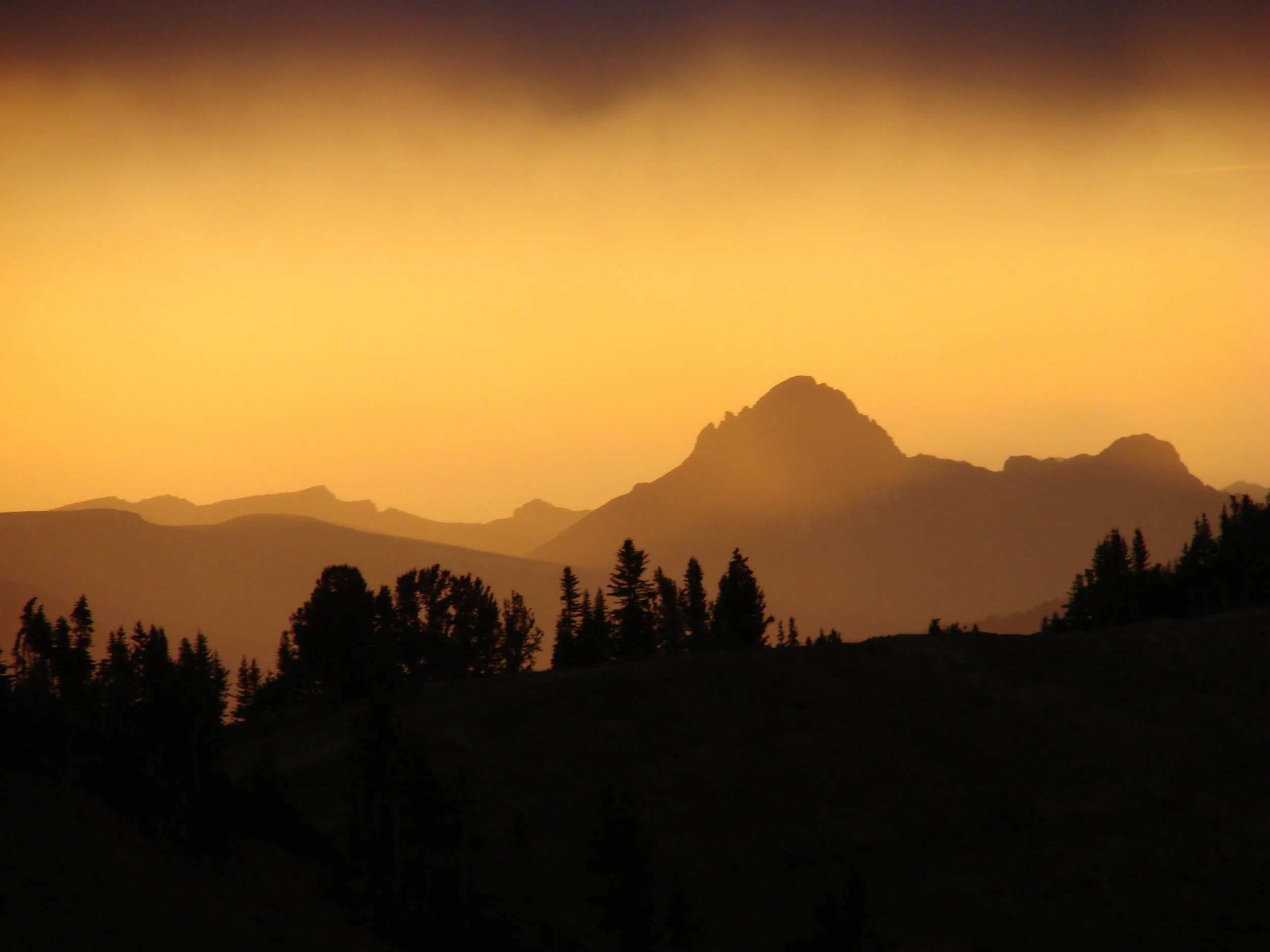 Silhouette of mountains and trees during sunset with a gradient orange-yellow sky.