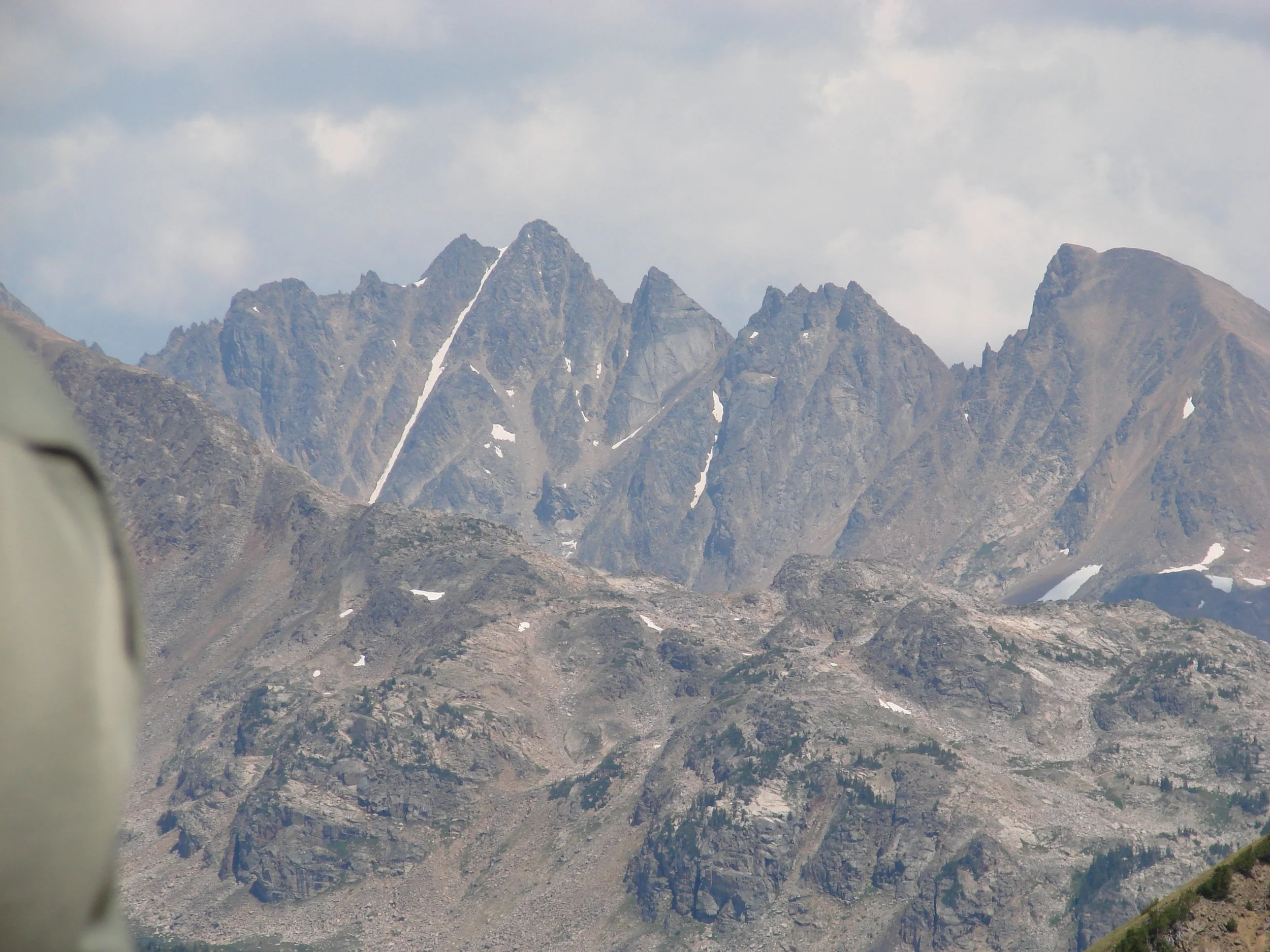 Mountain range with jagged peaks and sparse snow patches under a cloudy sky.