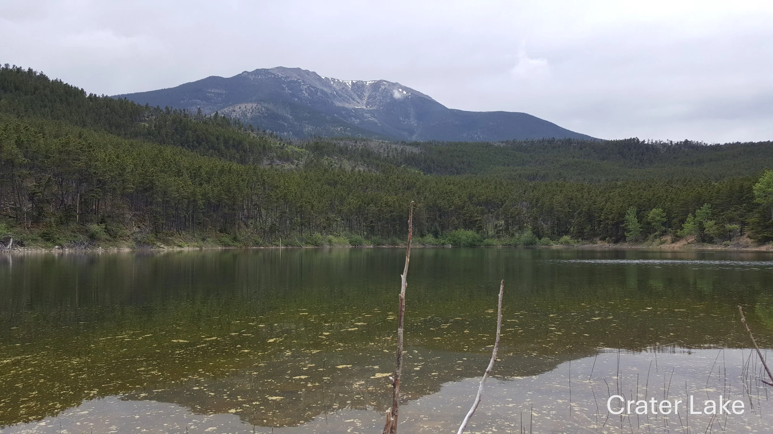 Mountain landscape with a lake and forested hills under a cloudy sky.