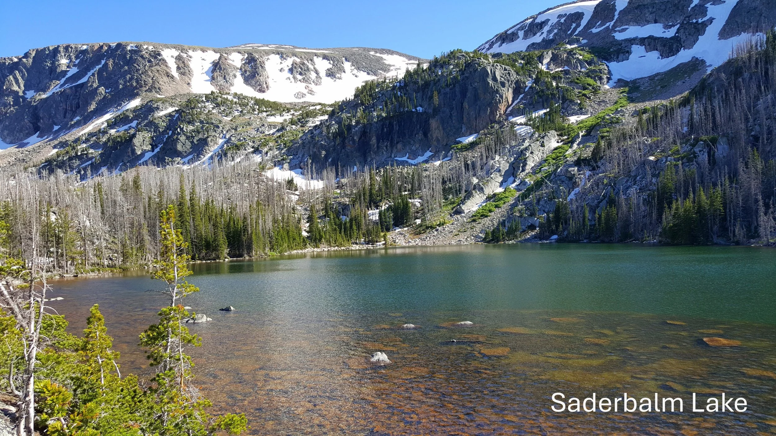 Mountain landscape with lake, trees, and snow-capped peaks labeled as Saderbalm Lake.