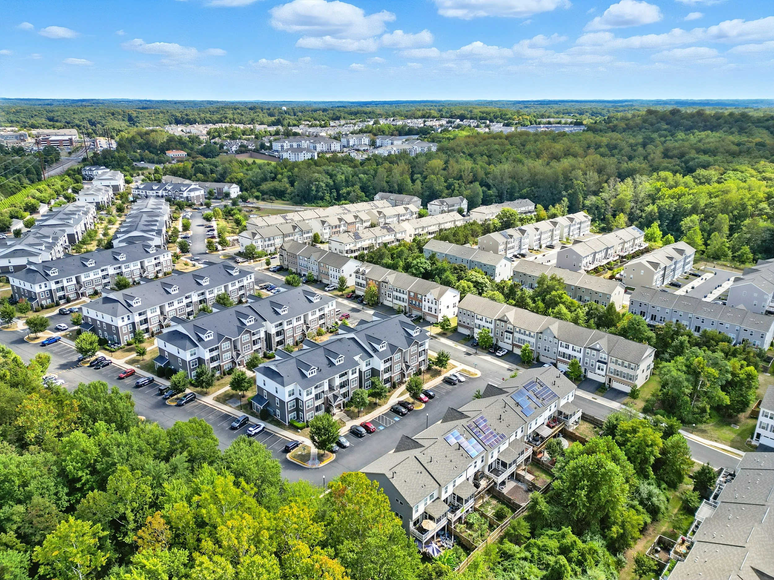 High aerial view of a dense suburban townhome community bordered by mature trees.