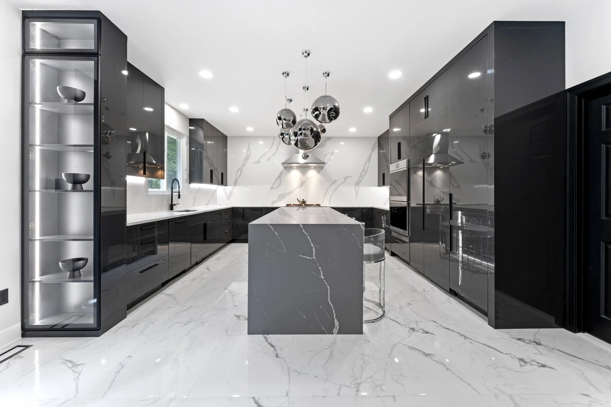 Modern black and white kitchen with marble flooring, marble island, black cabinetry, and a metallic pendant light fixture.