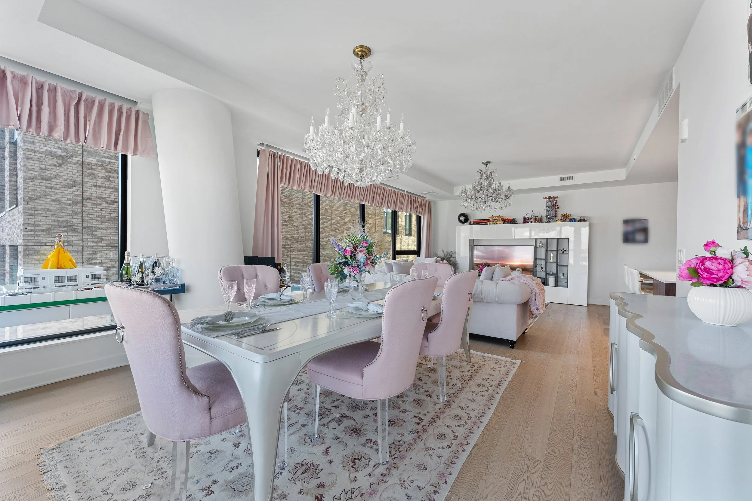 Wide open-plan dining and living room in an apartment unit with crystal chandeliers, pale wood floors and city windows