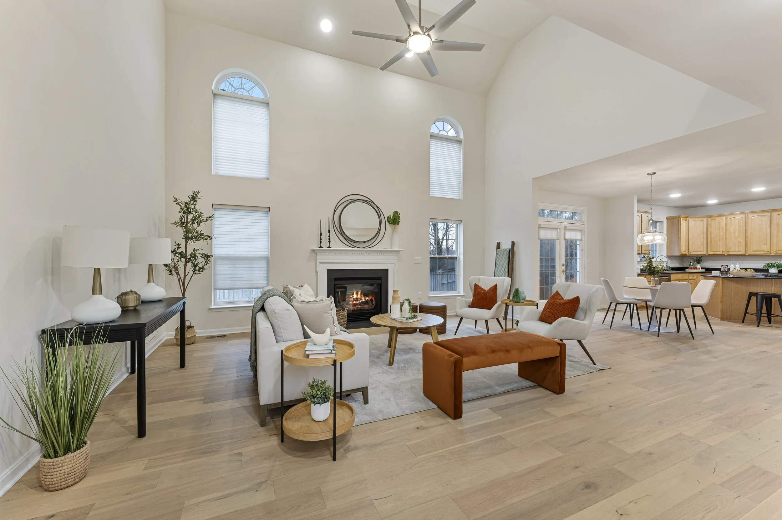 Living room with high vaulted ceiling, fireplace, multiple large windows, and modern furniture including sofas, armchairs, and side tables.