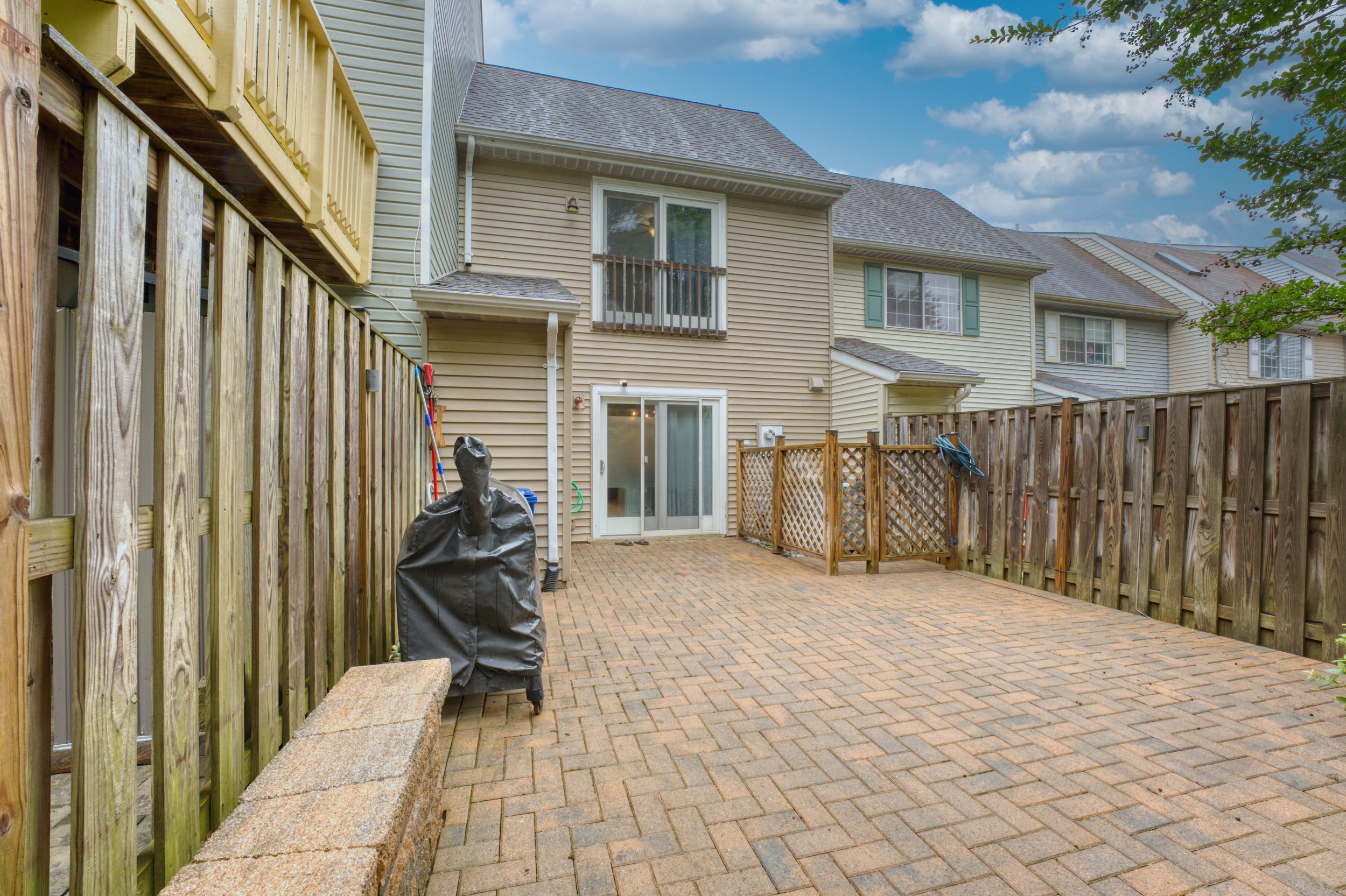 Fenced brick paver patio behind an attached townhome with a covered grill, a sliding glass door and a row of similar units behind it