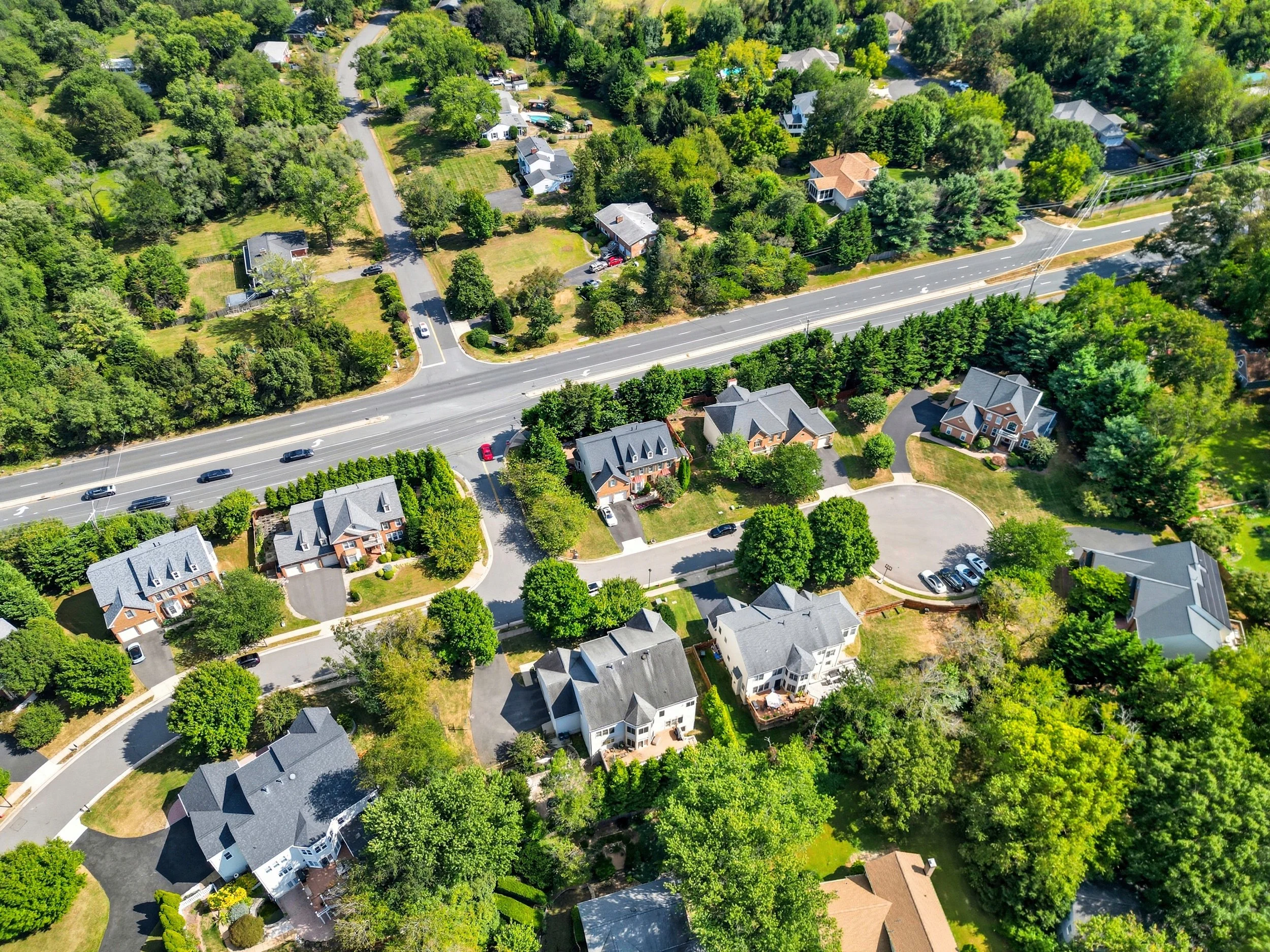 Aerial view of a suburban neighborhood showing a cul-de-sac, single-family homes, mature trees, and a divided highway.