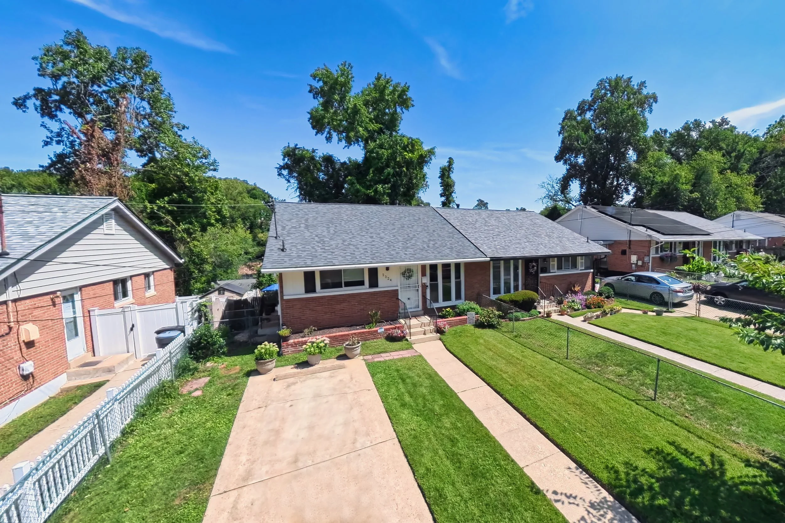 Elevated exterior view of a brick rambler and its front lawn on a clear day, captured from a mast