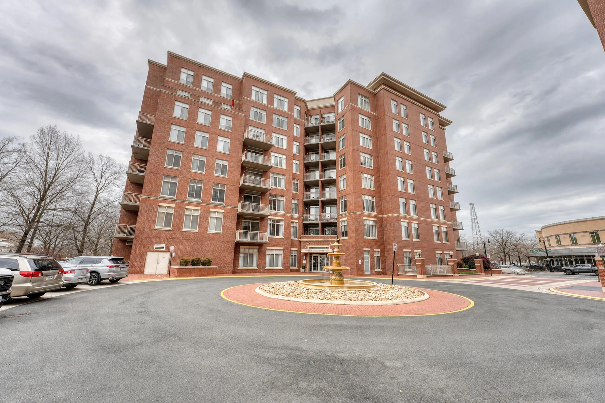 Mid-rise brick condominium building with a fountain courtyard, photographed under flat gray overcast with fully bare trees.