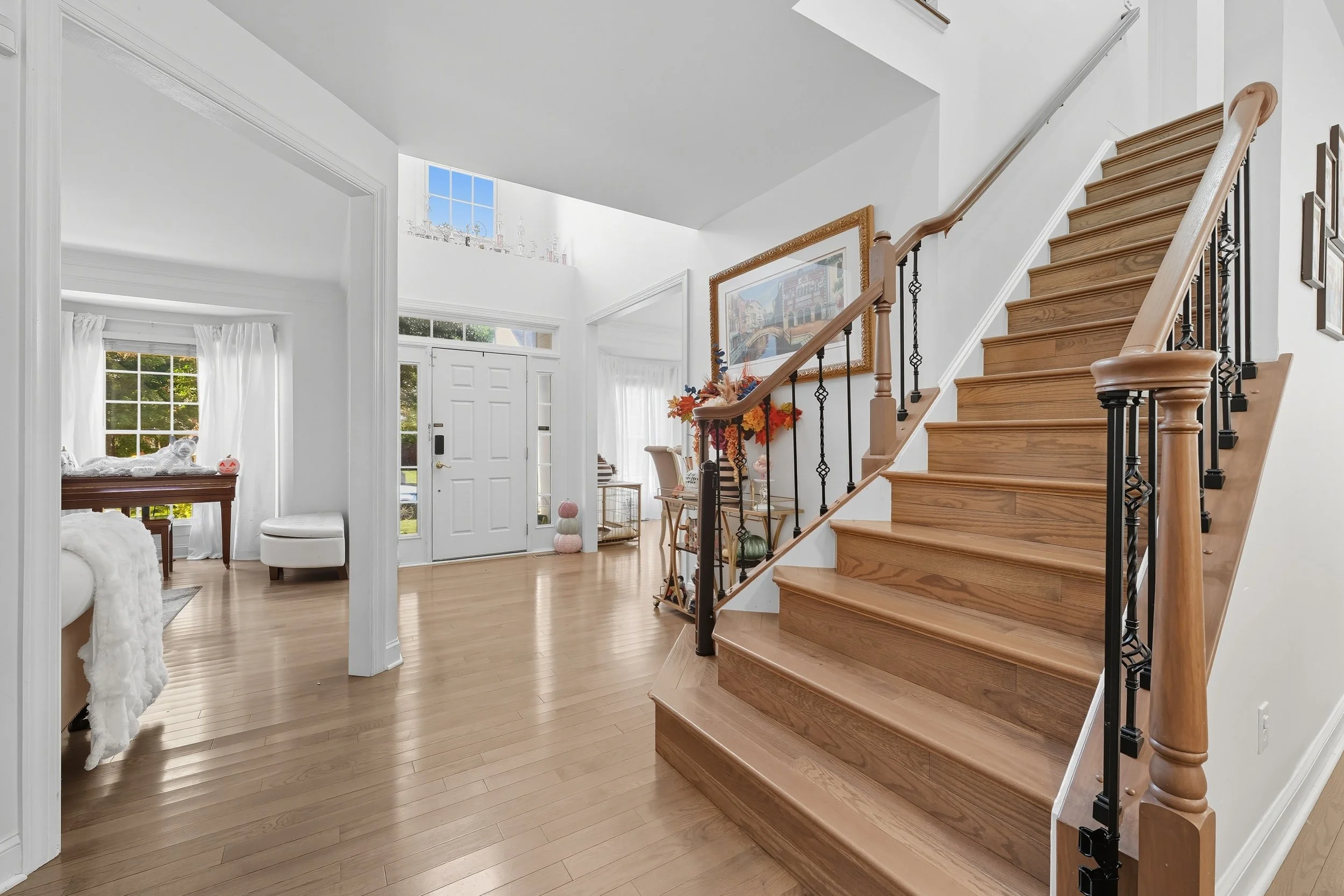 Two-story entry with a white front door, sidelights, and a wood staircase with black iron balusters over warm oak floors.