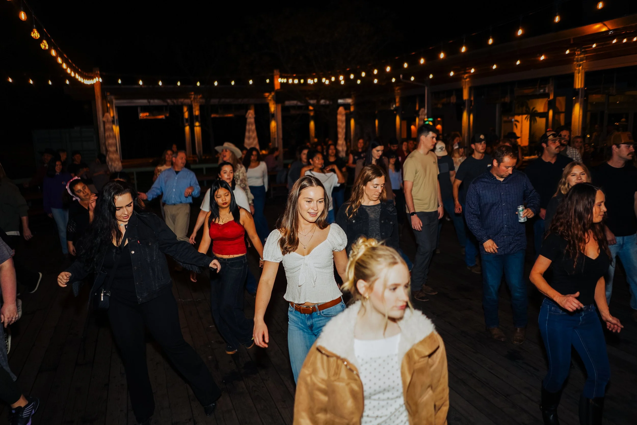 People dancing outdoors at night under string lights.