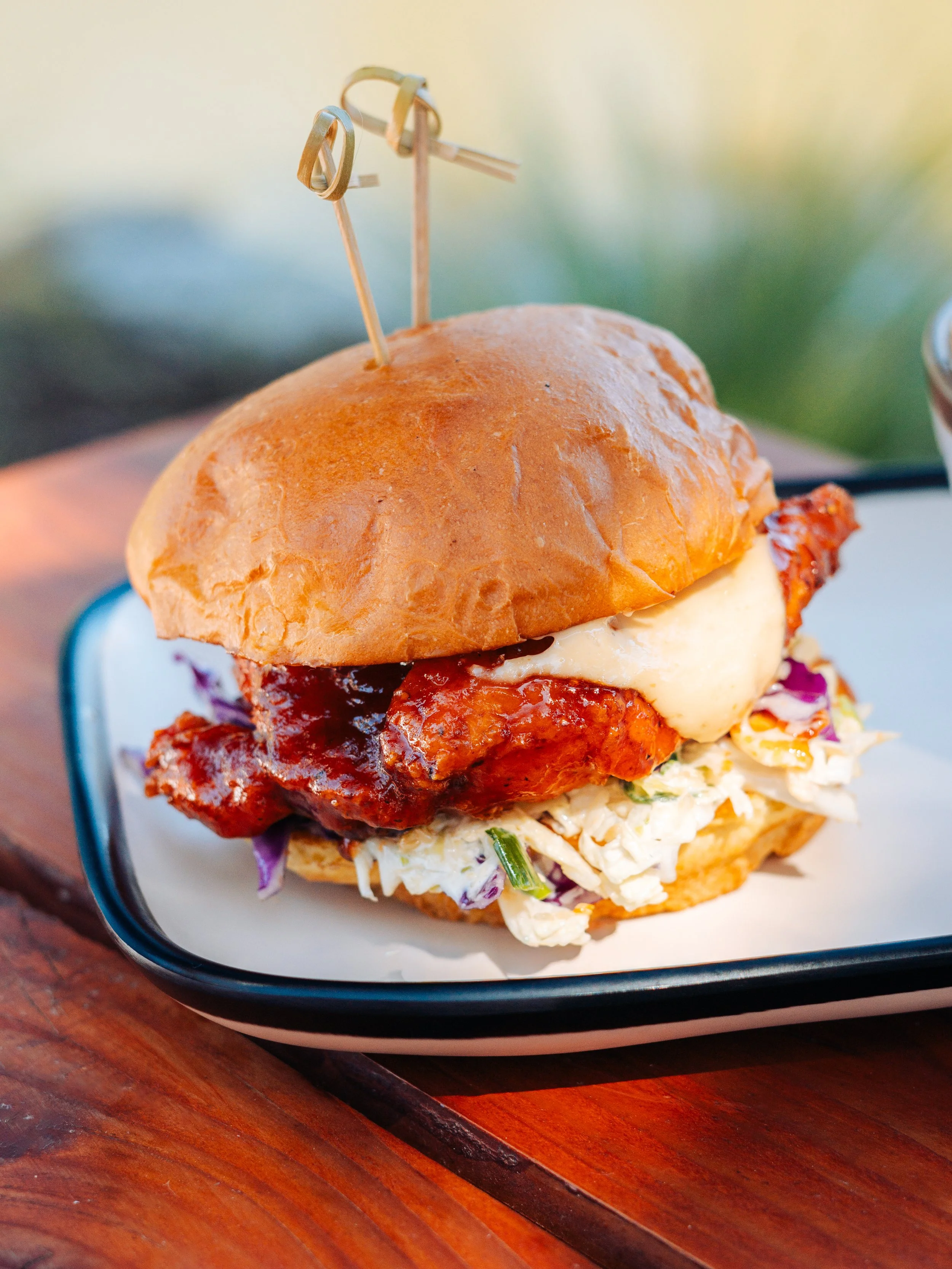 Close-up of a slider sandwich with fried chicken, coleslaw, and a bun, served on a black tray.