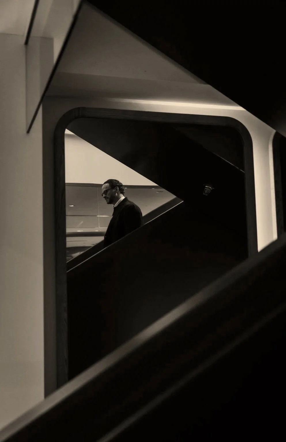 Man in a suit and glasses walking up a staircase, seen through a geometric framing