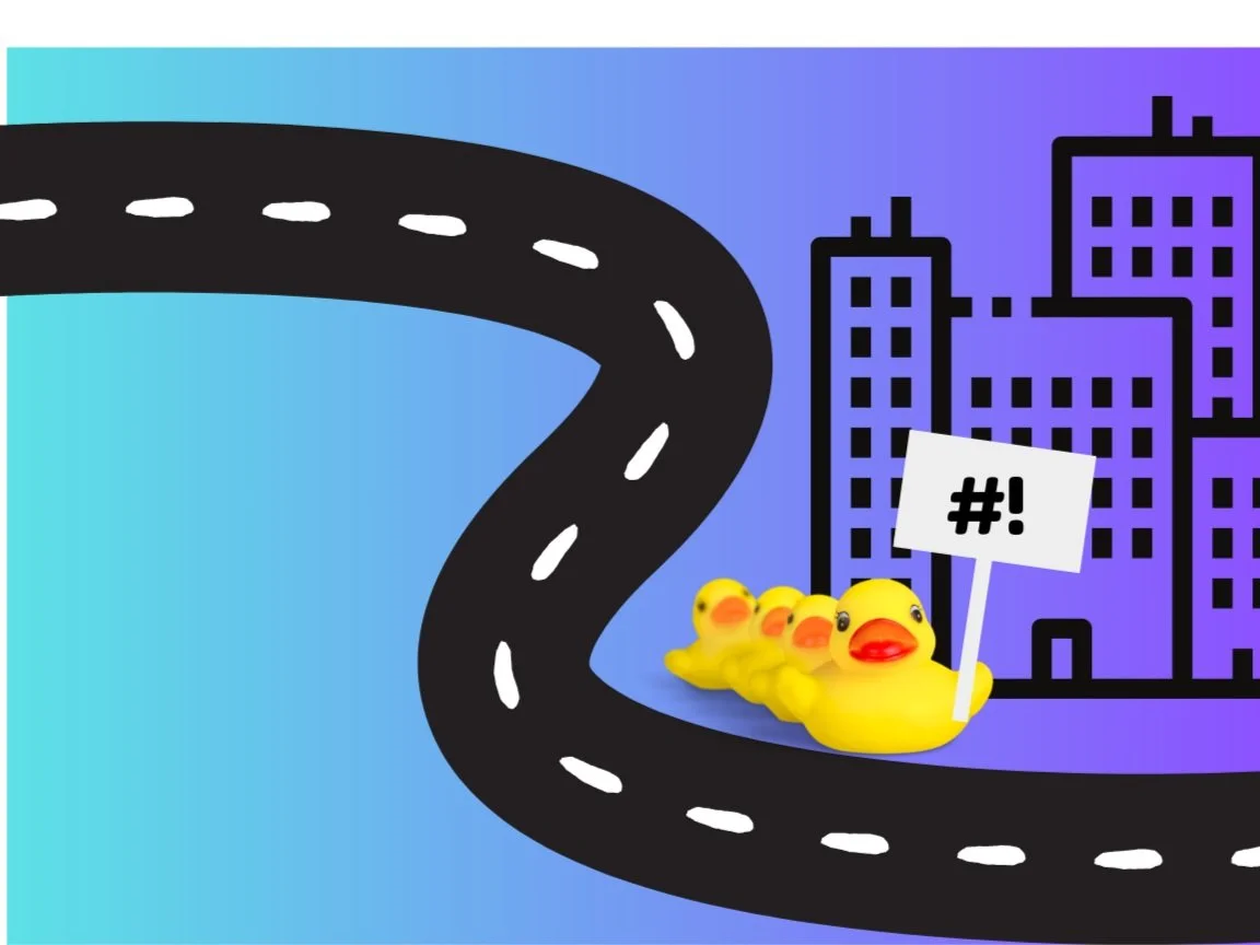Rubber duckies in a row holding a sign, next to a road in a city.