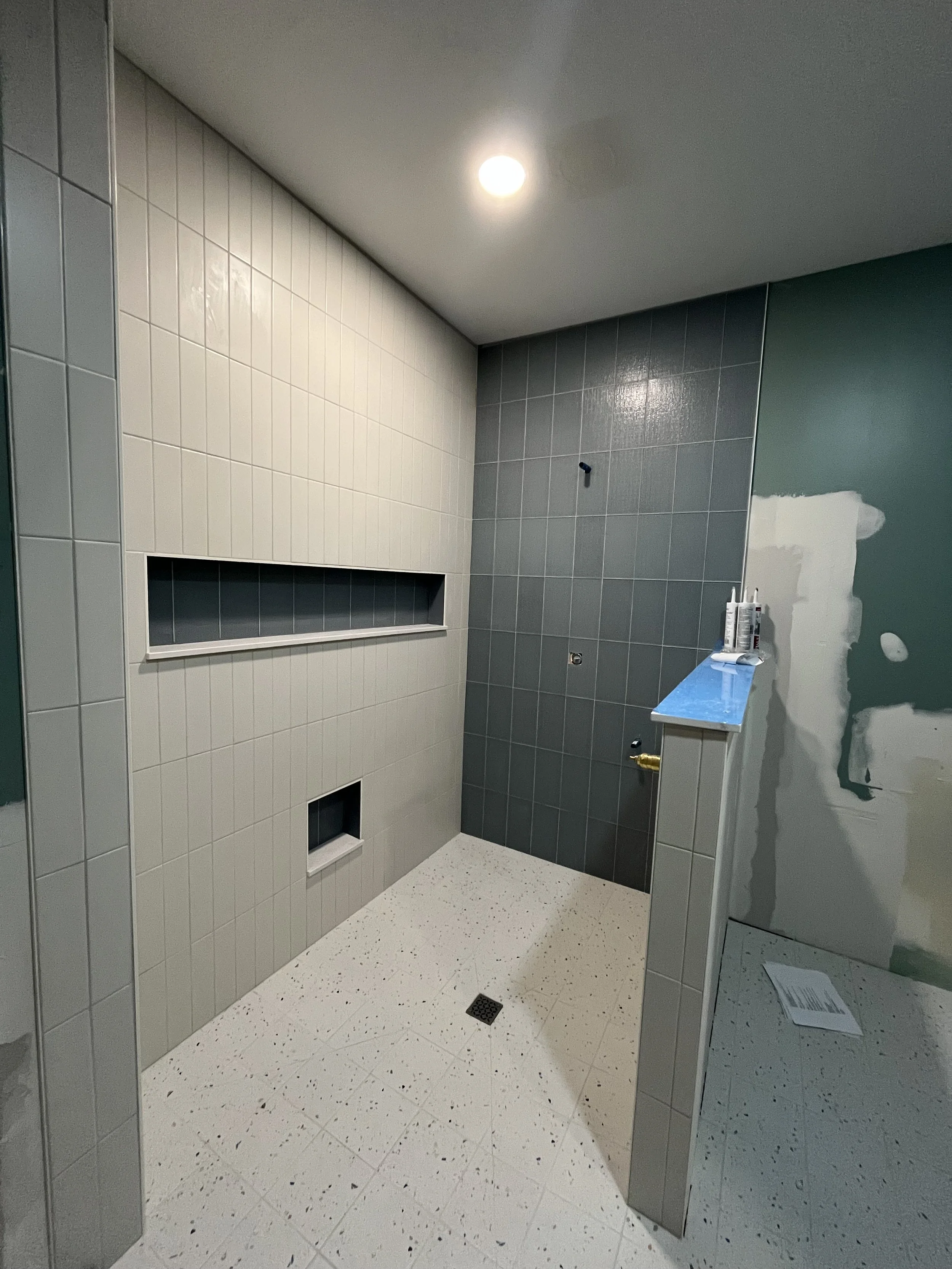 Gray tiled zero curb walk-in shower with a built-in tile shelf, showerhead, and safety grab bars.