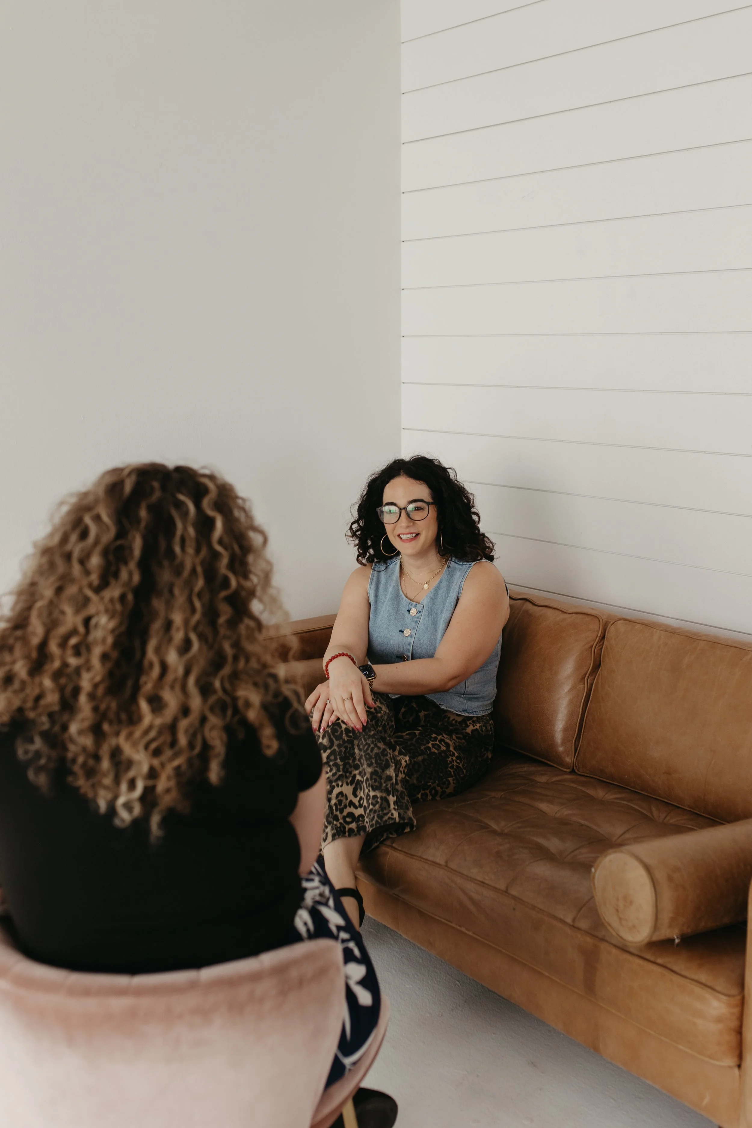 Carly Shadid, LMFT, seated on a leather couch talking with a client during an individual therapy session