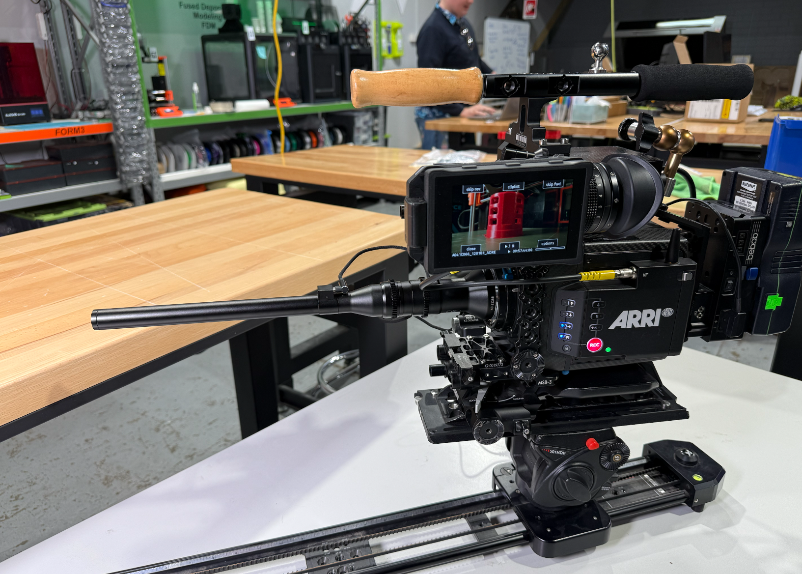 Professional ARRI film camera mounted on a dolly, positioned on a wooden table in a workshop or studio environment with tools and shelving in the background.