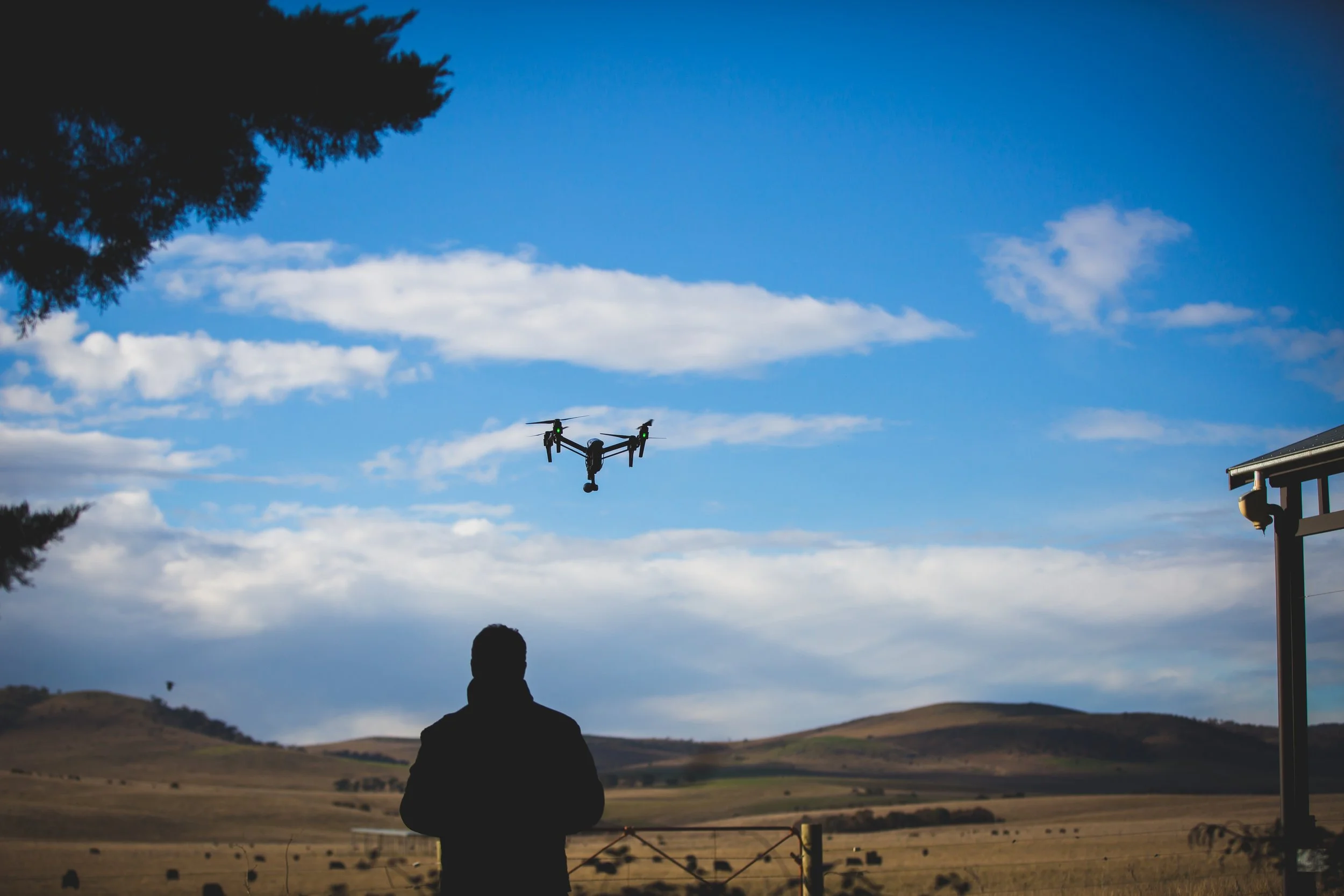 Person flying a drone over an open landscape with hills and a blue sky with clouds.