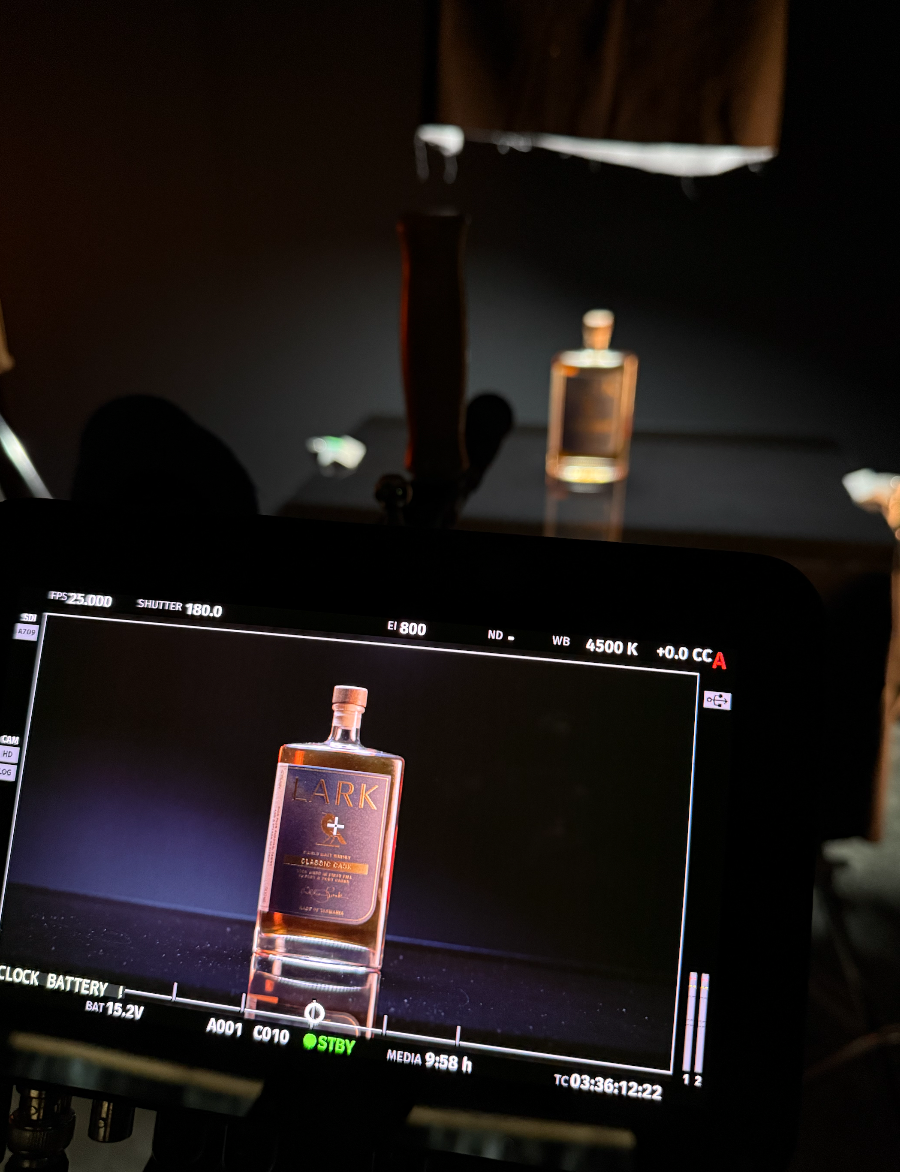 Photograph of a product shot of a bottle labeled 'LARK' on a monitor screen, with the actual bottle and another object blurred in the background.