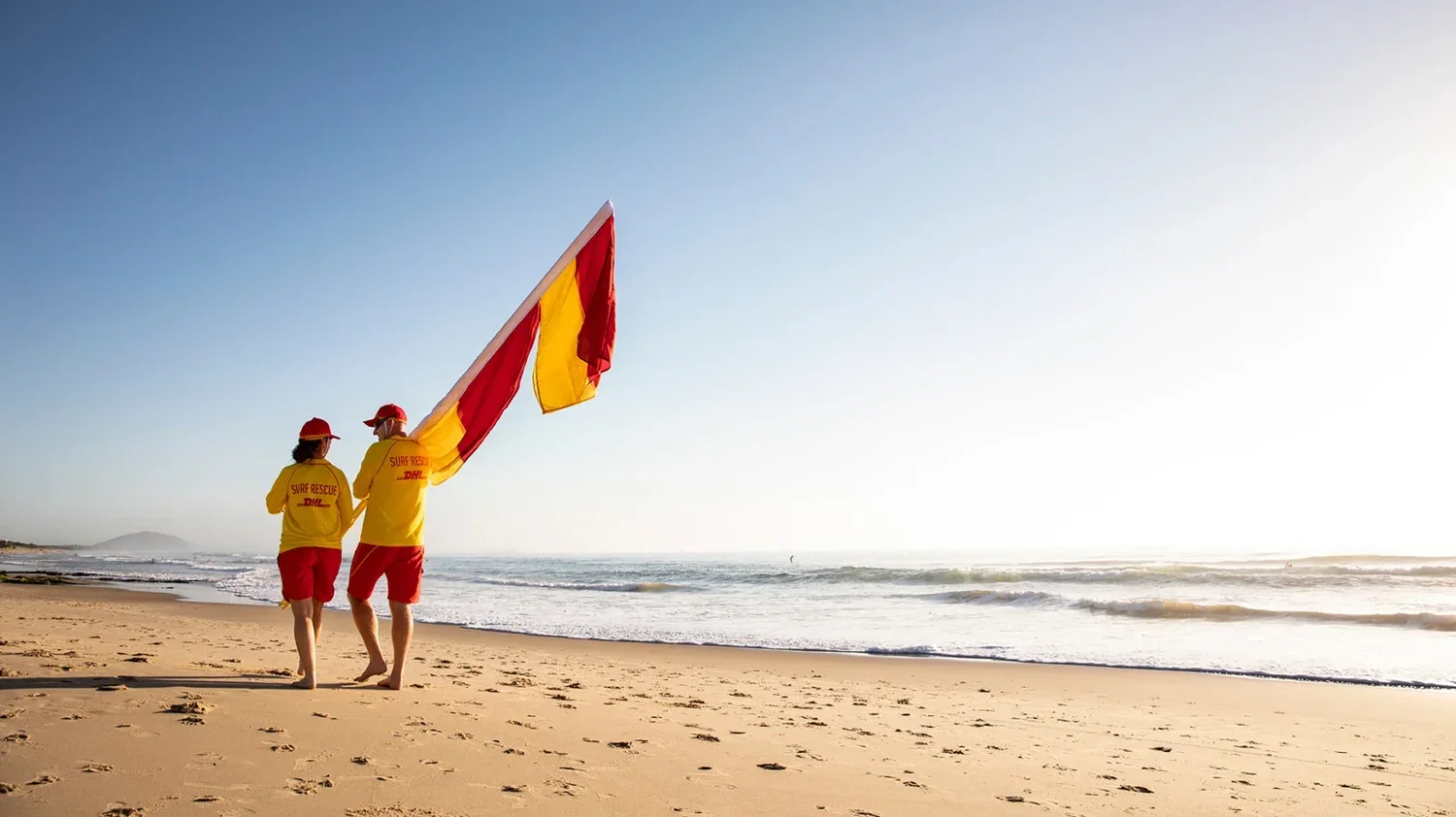 Lifesavers carrying red and yellow patrol flags on a beach