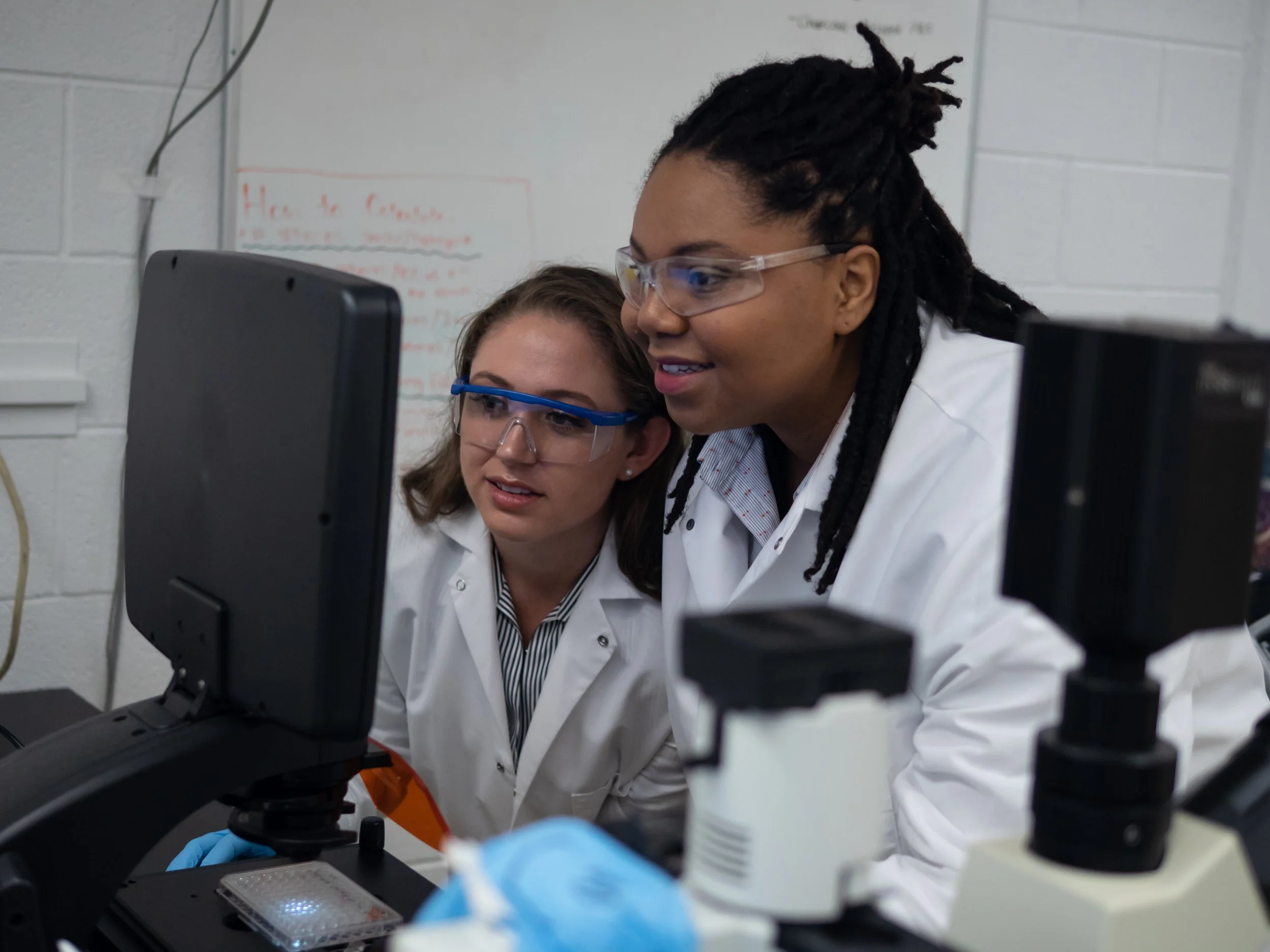 Two scientists wearing lab coats and safety goggles working with lab equipment in a laboratory.