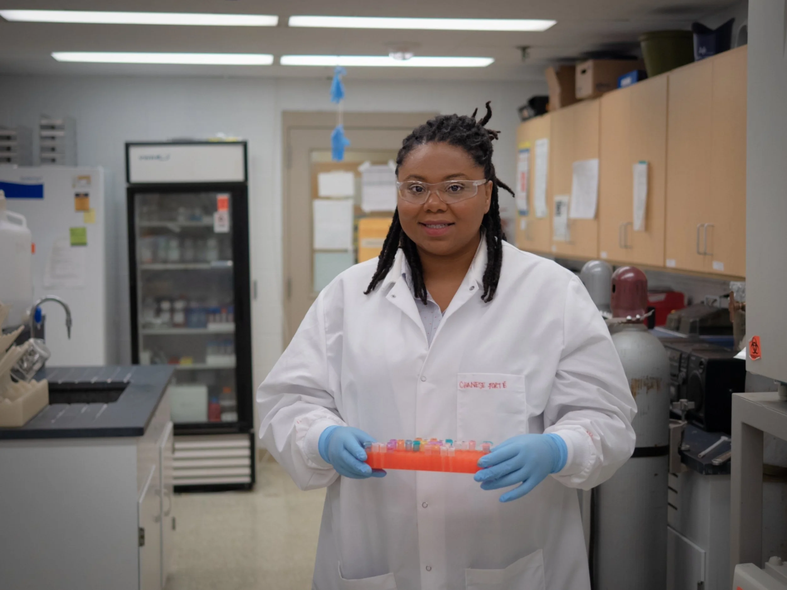 Scientist in a lab holding test tubes, wearing a lab coat and gloves