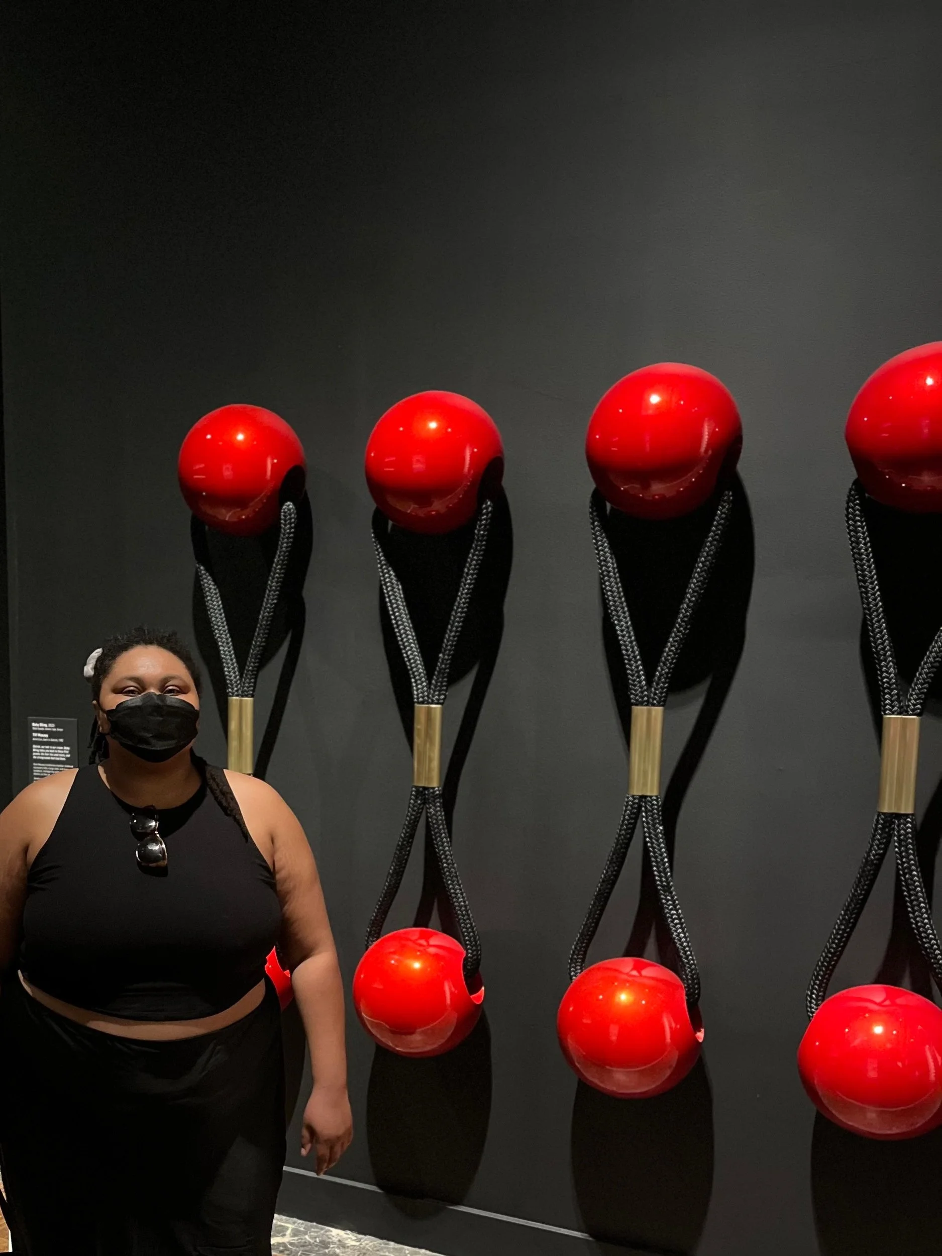 Person standing in front of a black wall with five red spherical objects mounted on it.