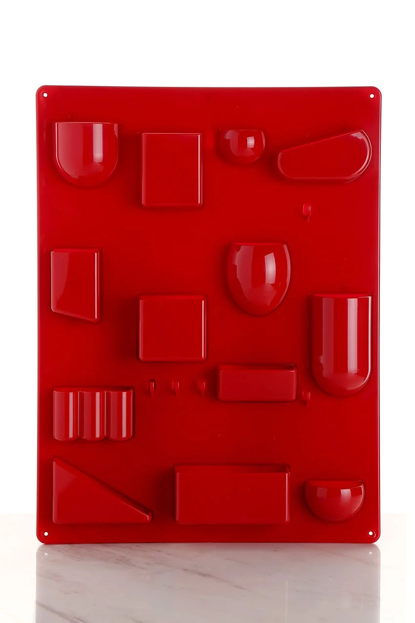 Red pegboard with various red 3D geometric shapes attached, displayed vertically on a white background.